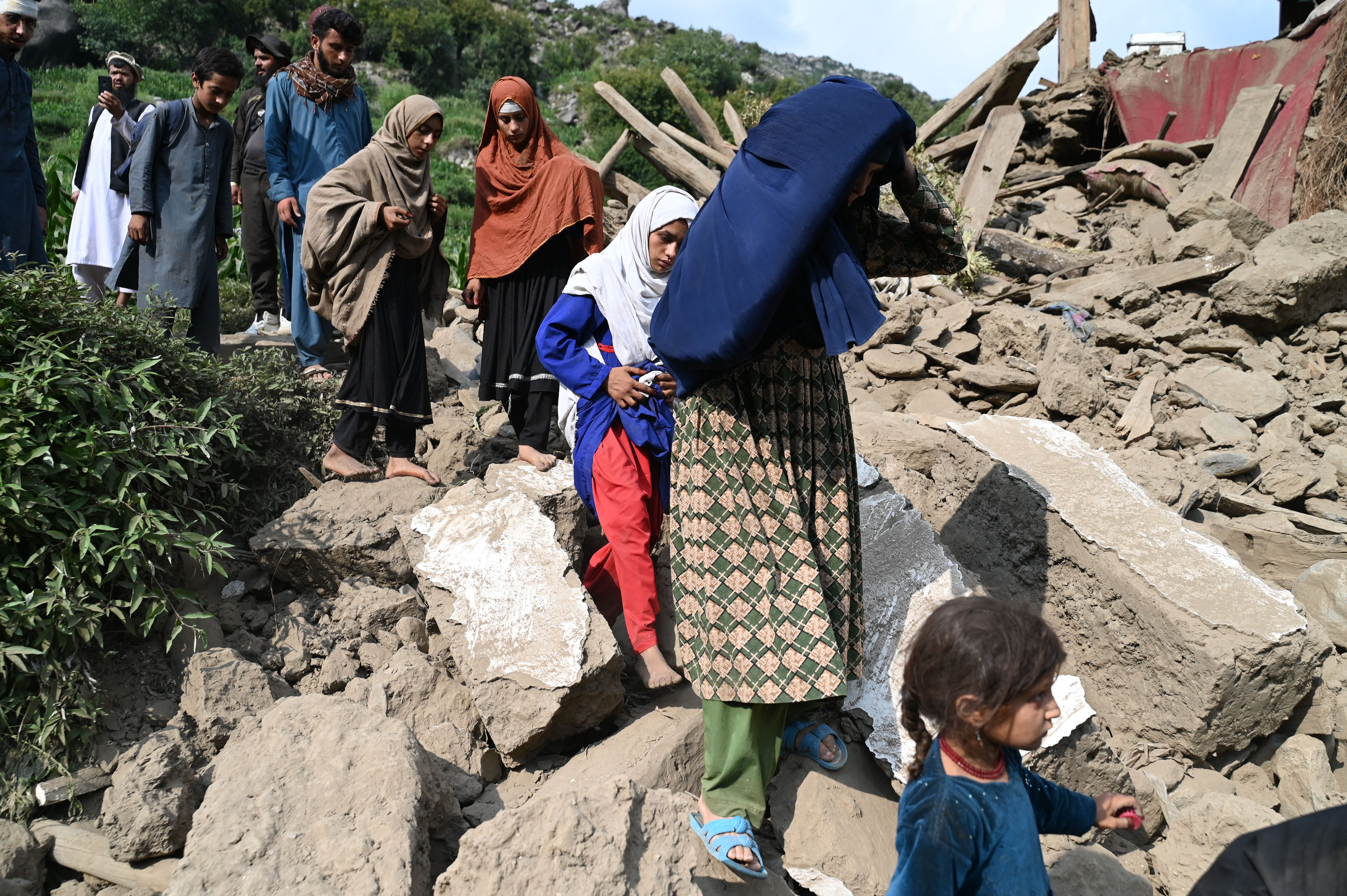 Men and women in traditional Afghan and Muslim dress step over rubble as they walk in single file.