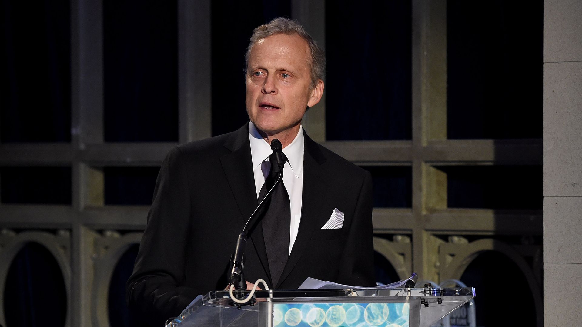 Photo of a man in front of a microphone and a podium. 