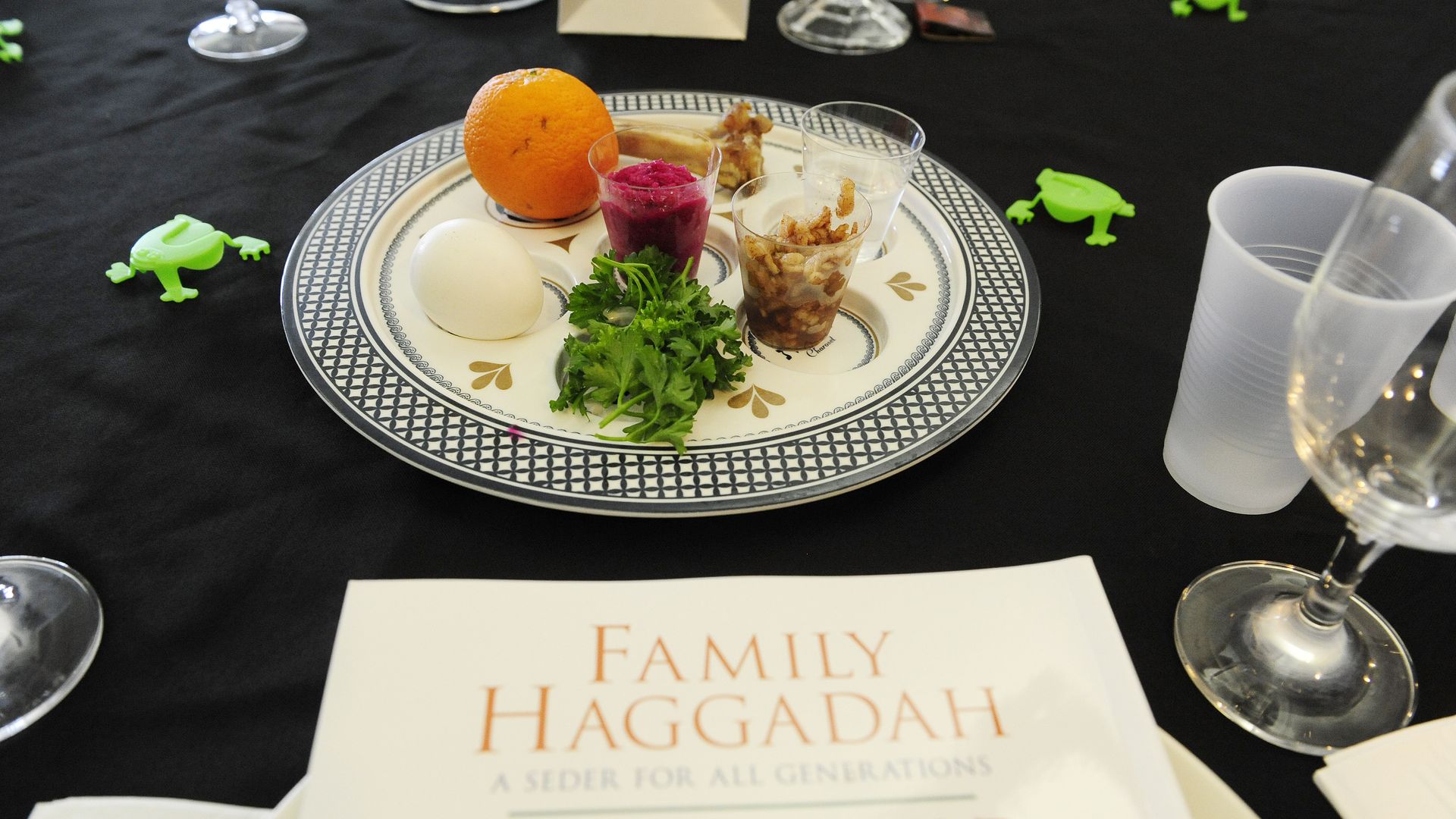 Passover Seder plate on a table with glasses and cups and Family Haggadah books