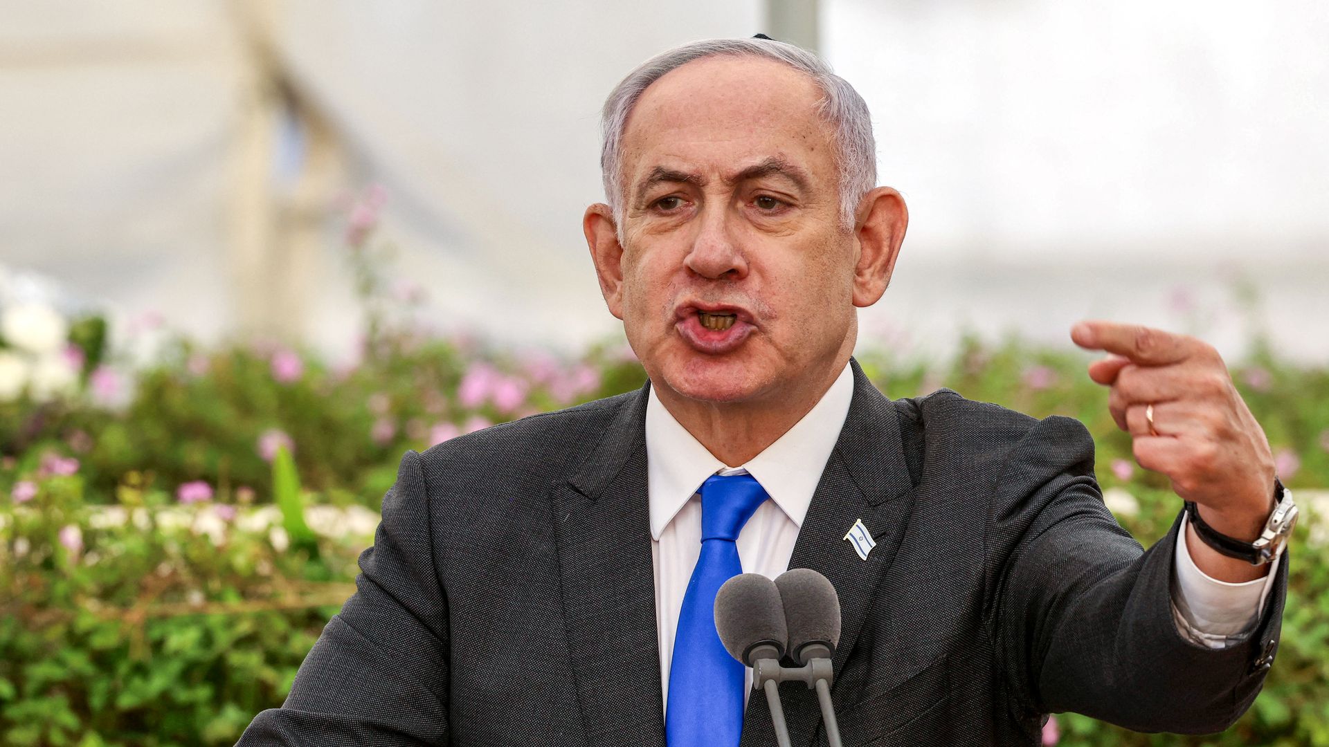 Benjamin Netanyahu, wearing a gray suit, white shirt and blue tie, points with his left index finger