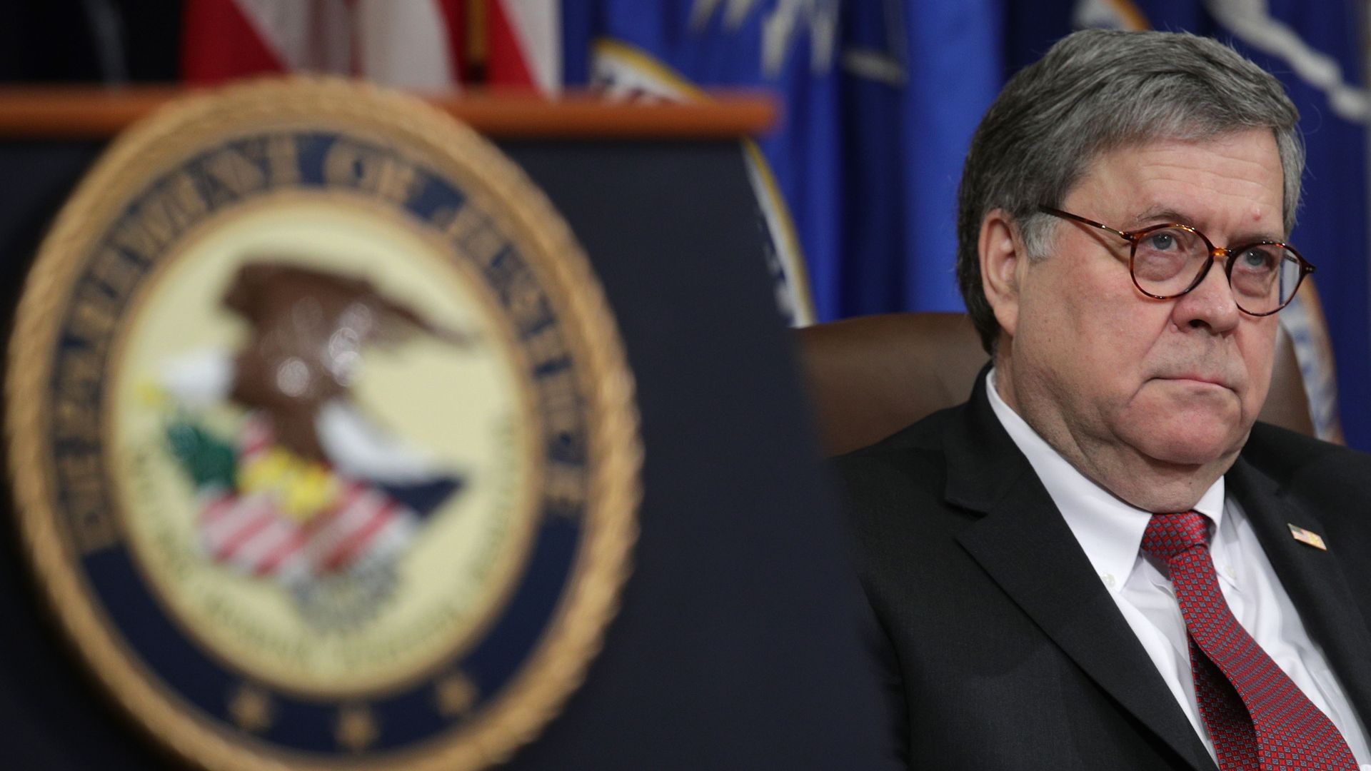In this image, William Barr sits in a suit and tie.
