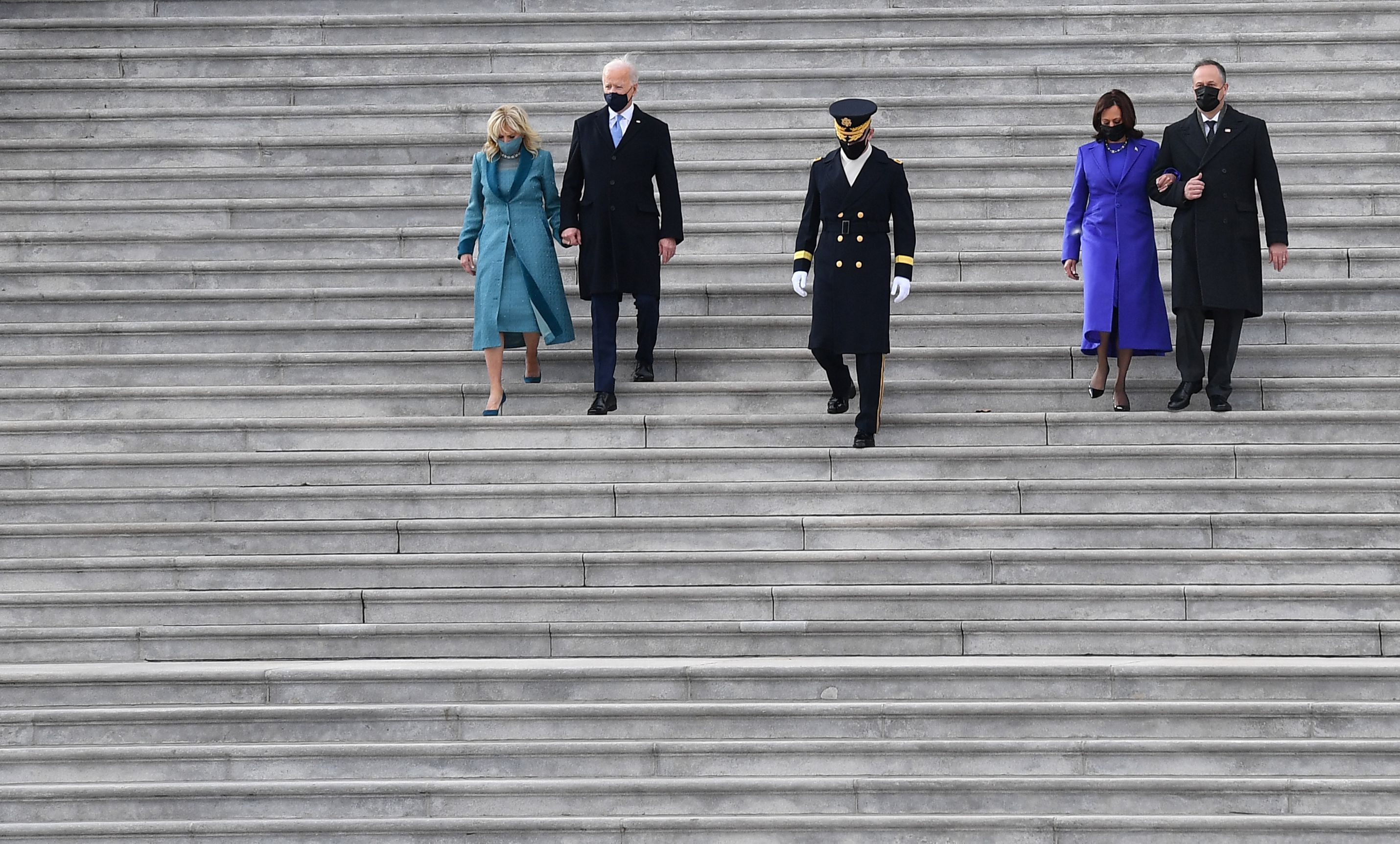 Photo of Joe Biden, Jill Biden, Kamala Harris and Doug Emhoff walking down the stairs with a soldier