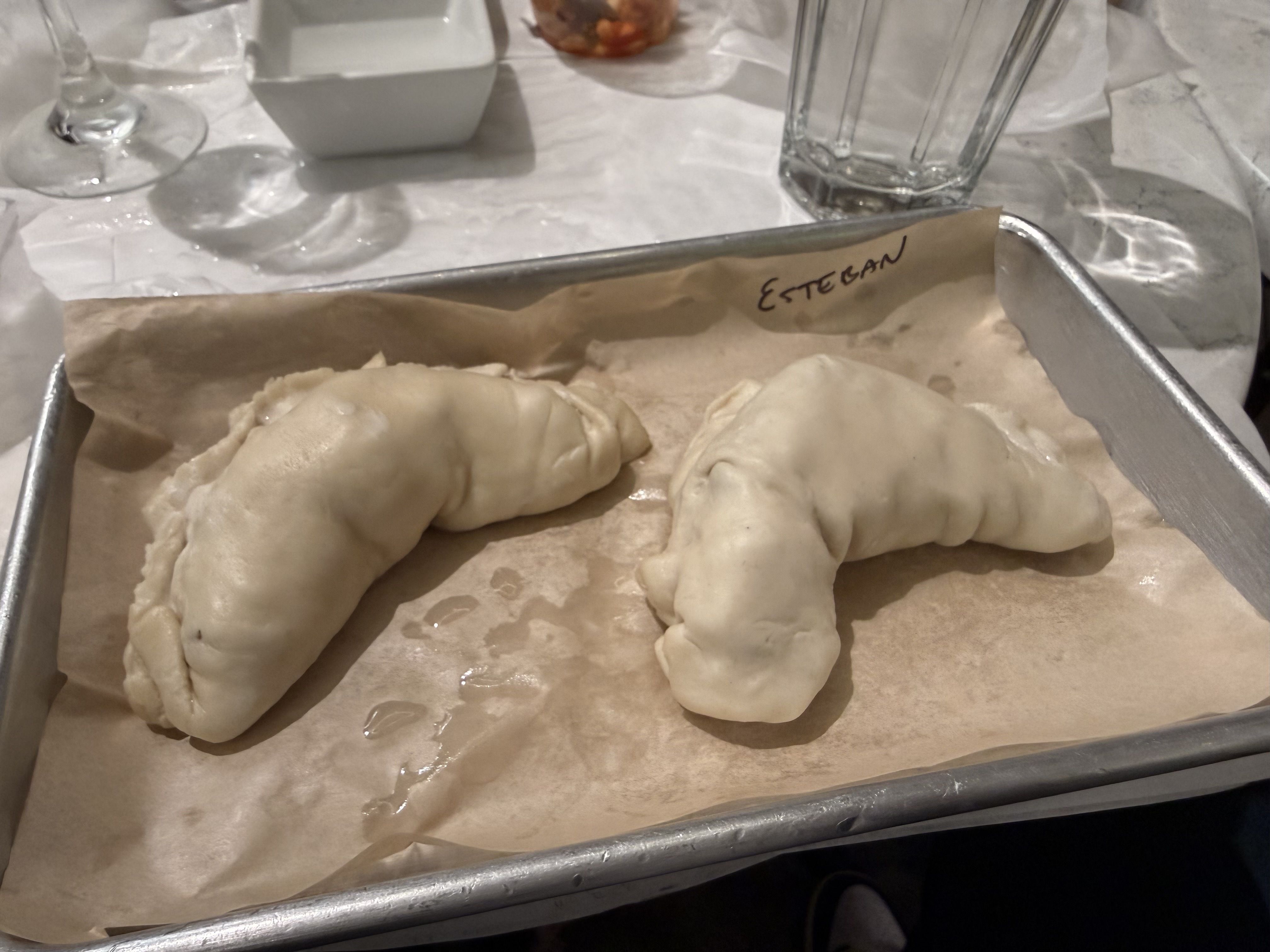 Two uncooked, folded dough empanadas on a baking sheet lined with parchment paper.