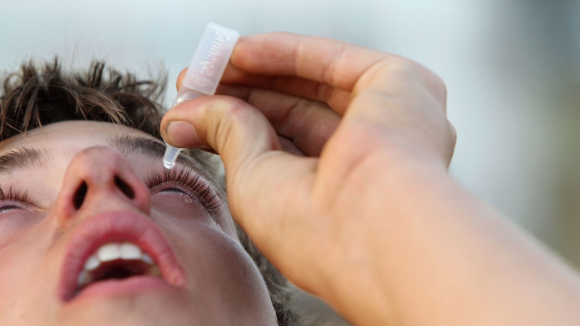 A man puts eye drops in his eye.