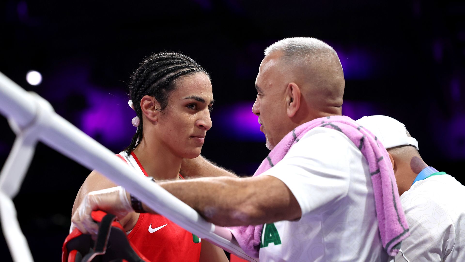 Algerian boxer Imane Khelif listens to a coach over the edge of a boxing ring.