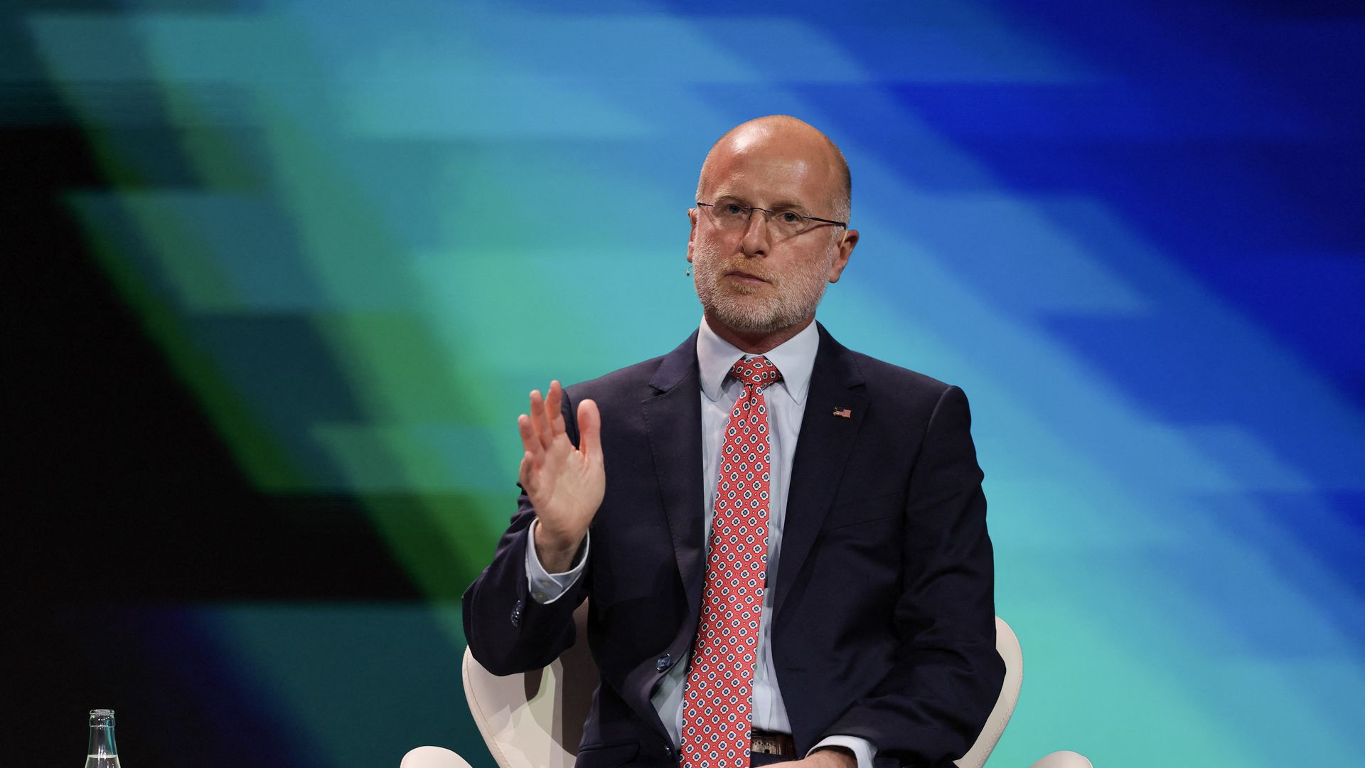 A person in a suit and tie gestures with their hand