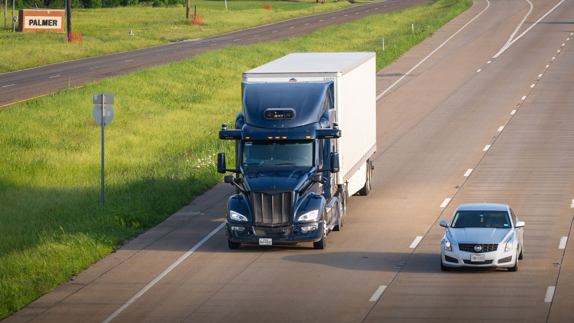 Image of an Aurora self-driving semi truck operating on a highway in Texas. Notably, the Peterbilt logo is covered, or removed from the truck's grille. 