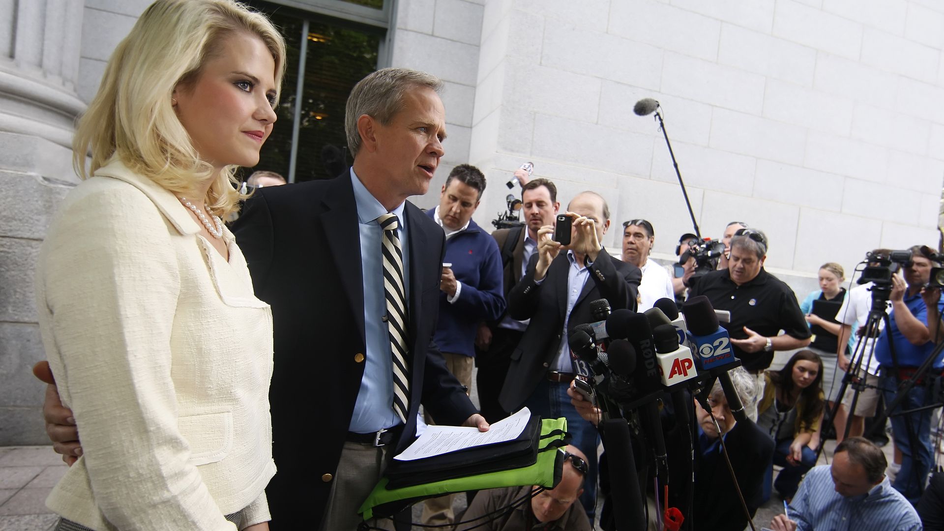 Blonde woman in front of press. 