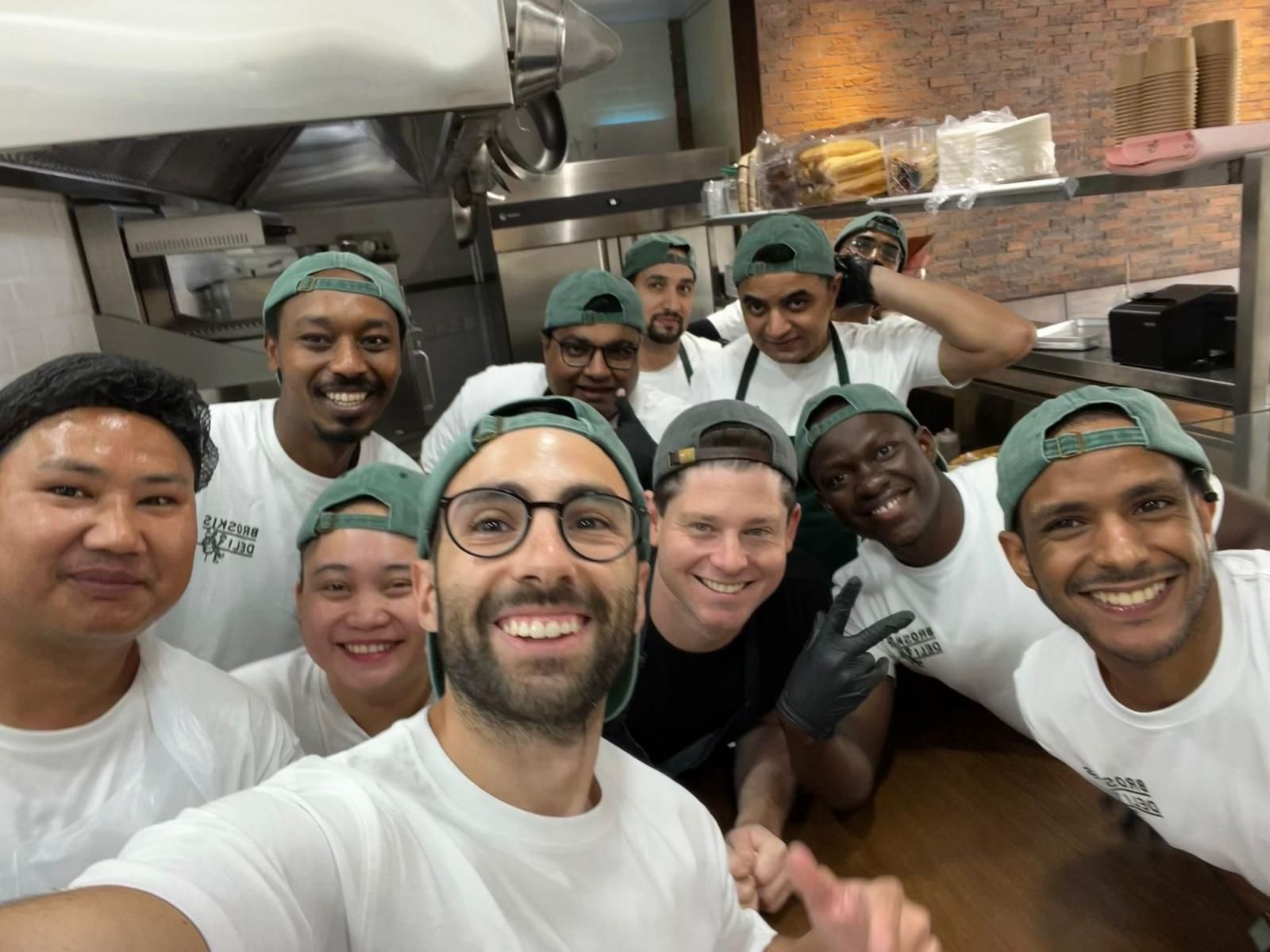 a group of chefs and restaurant workers wearing white t-shirts and backwards green hats
