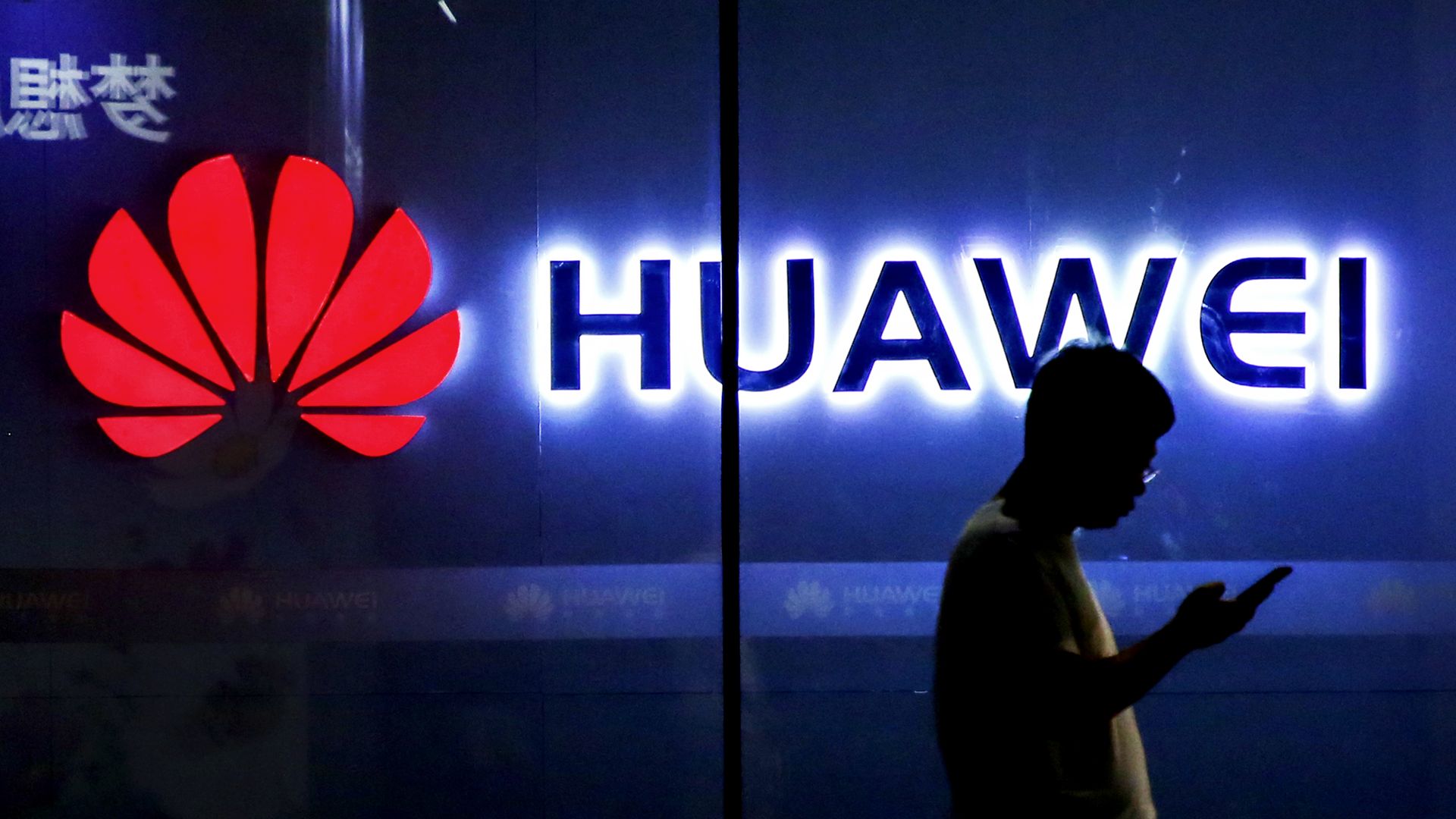 Photo of man using a smartphone silhouetted against a glowing Huawei logo
