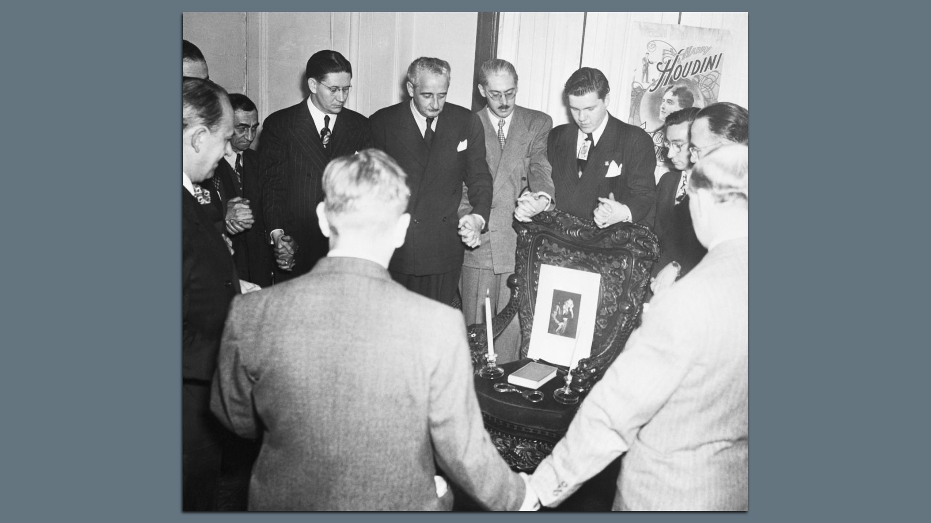 Men in suits holding hands in a circle. A chair in the center contains items from Houdini
