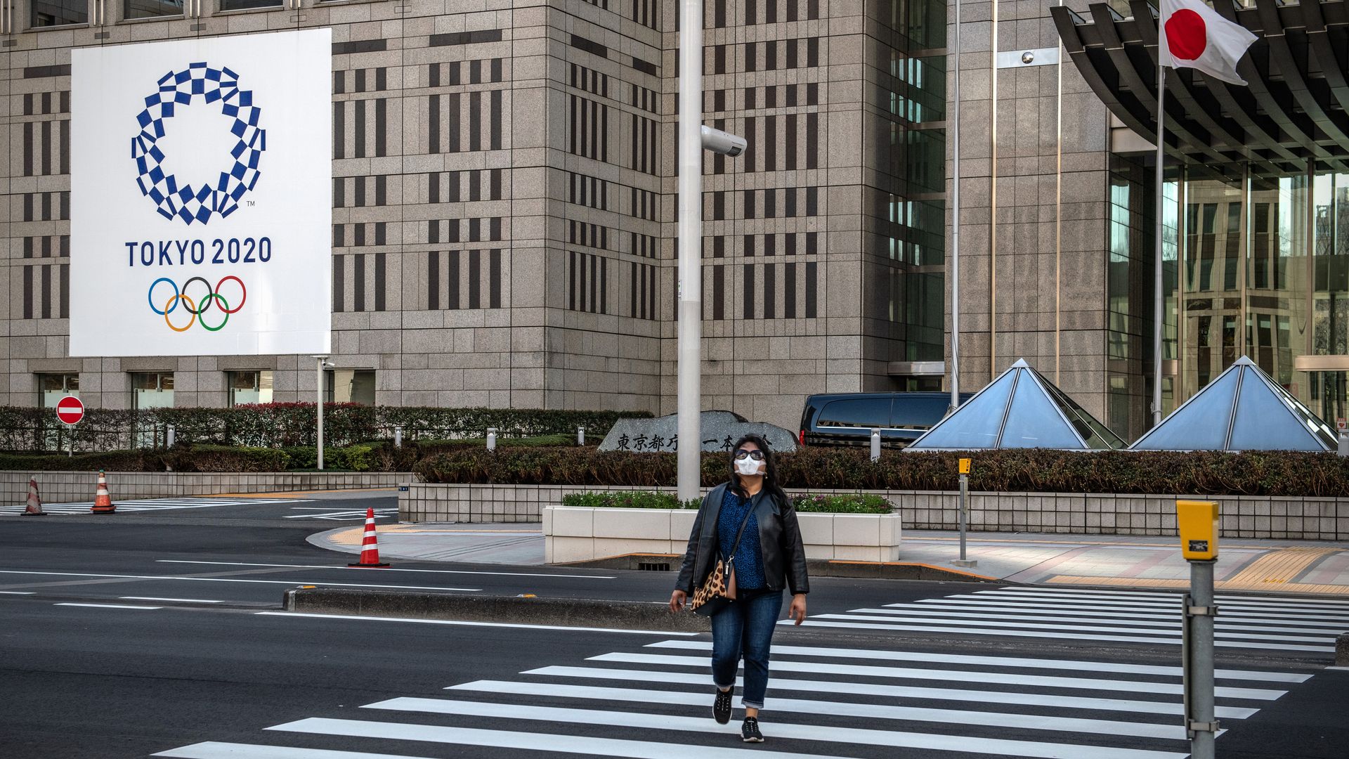 A woman wearing a face mask walks past a Tokyo 2020 Olympics banner displayed on the side of a building on March 19, 2020 in Tokyo, Japan. 