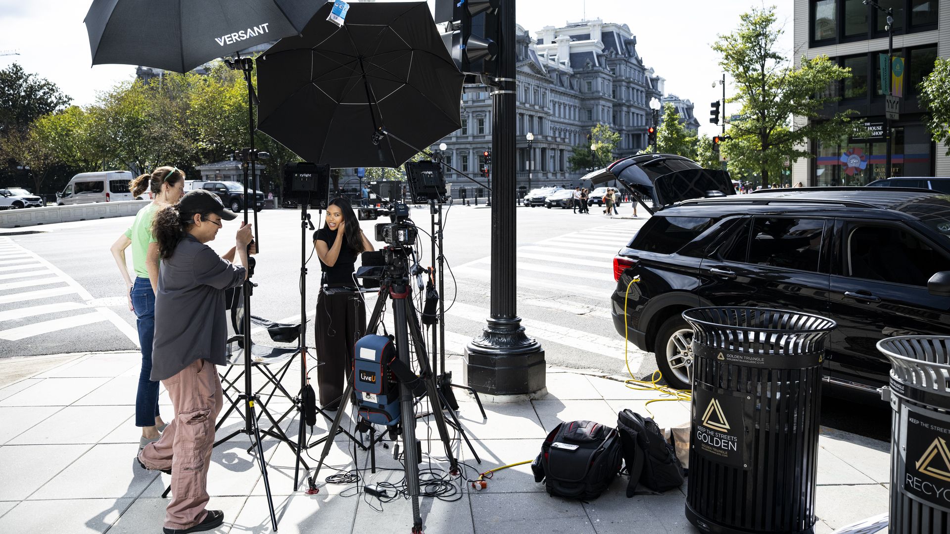 A reporter under umbrellas on a street corner preparing for a TV report.