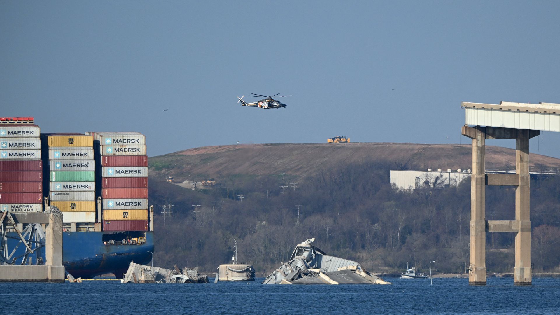 The remains of the collapsed Francis Scott Key Bridge lie in the Patapsco River after the container ship Dali (L) struck it on March 26, in Baltimore, Maryland, on March 29, 2024, as clean-up work begins.