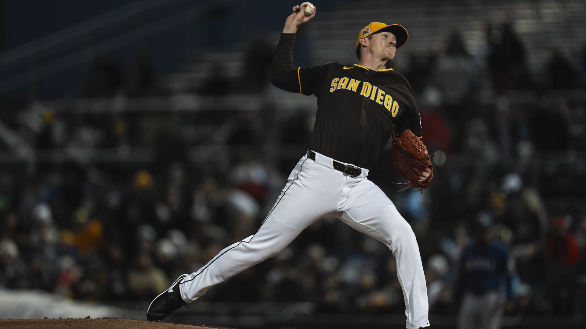Nick Pivetta pitching in a brown padres jersey in front of a sparse spring training crowd at night