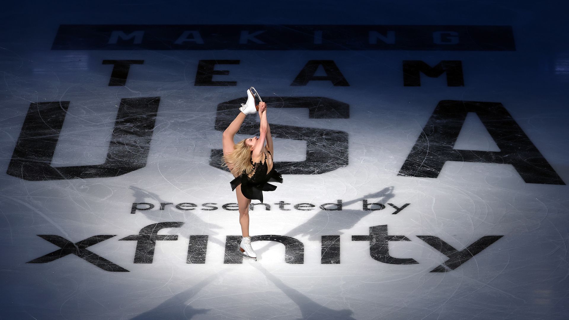 Figure skater Amber Glenn is spotlighted as she spins on ice with large "TEAM USA" and "presented by xfinity" logos beneath her.