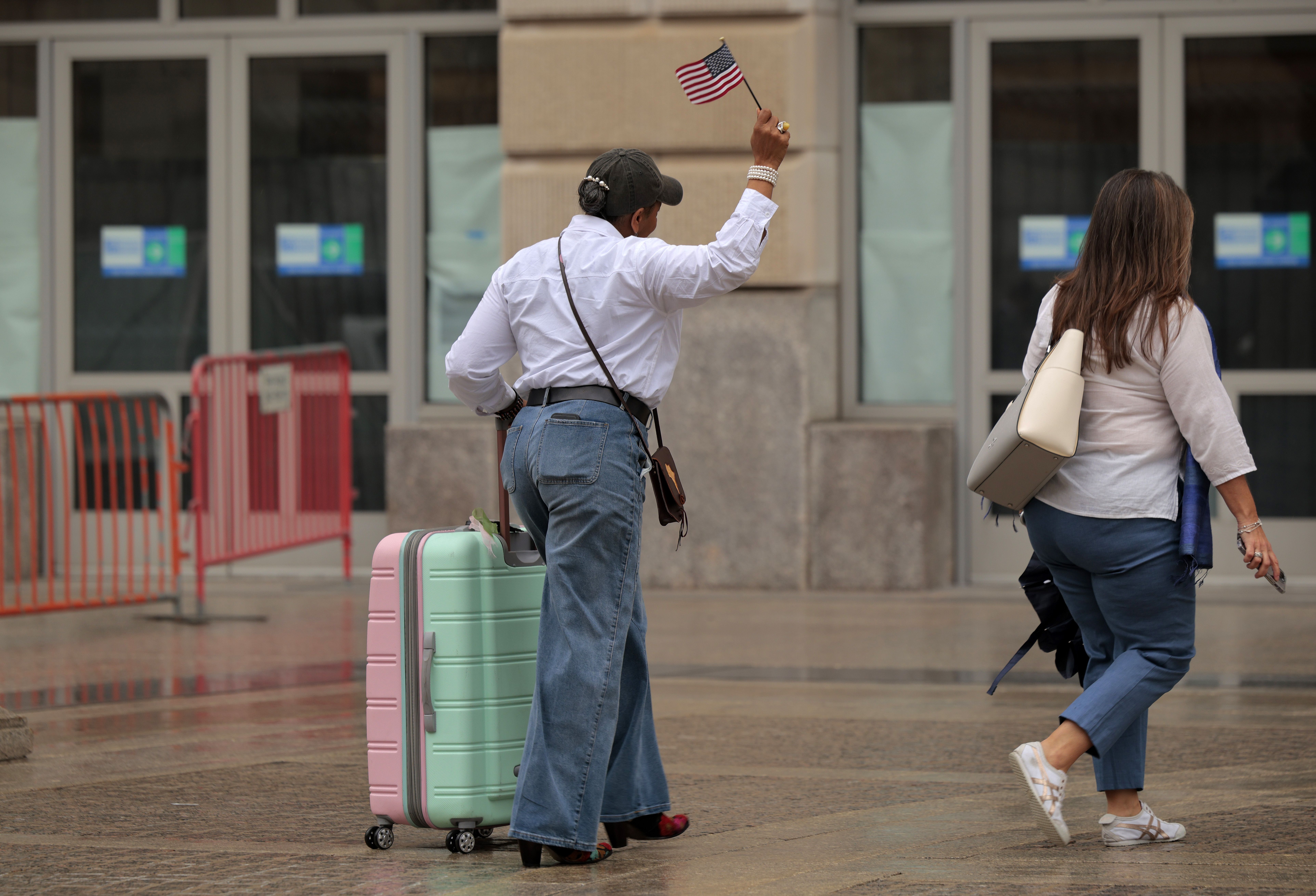 A woman holding an American flag and pulling a suitcase outside USAID