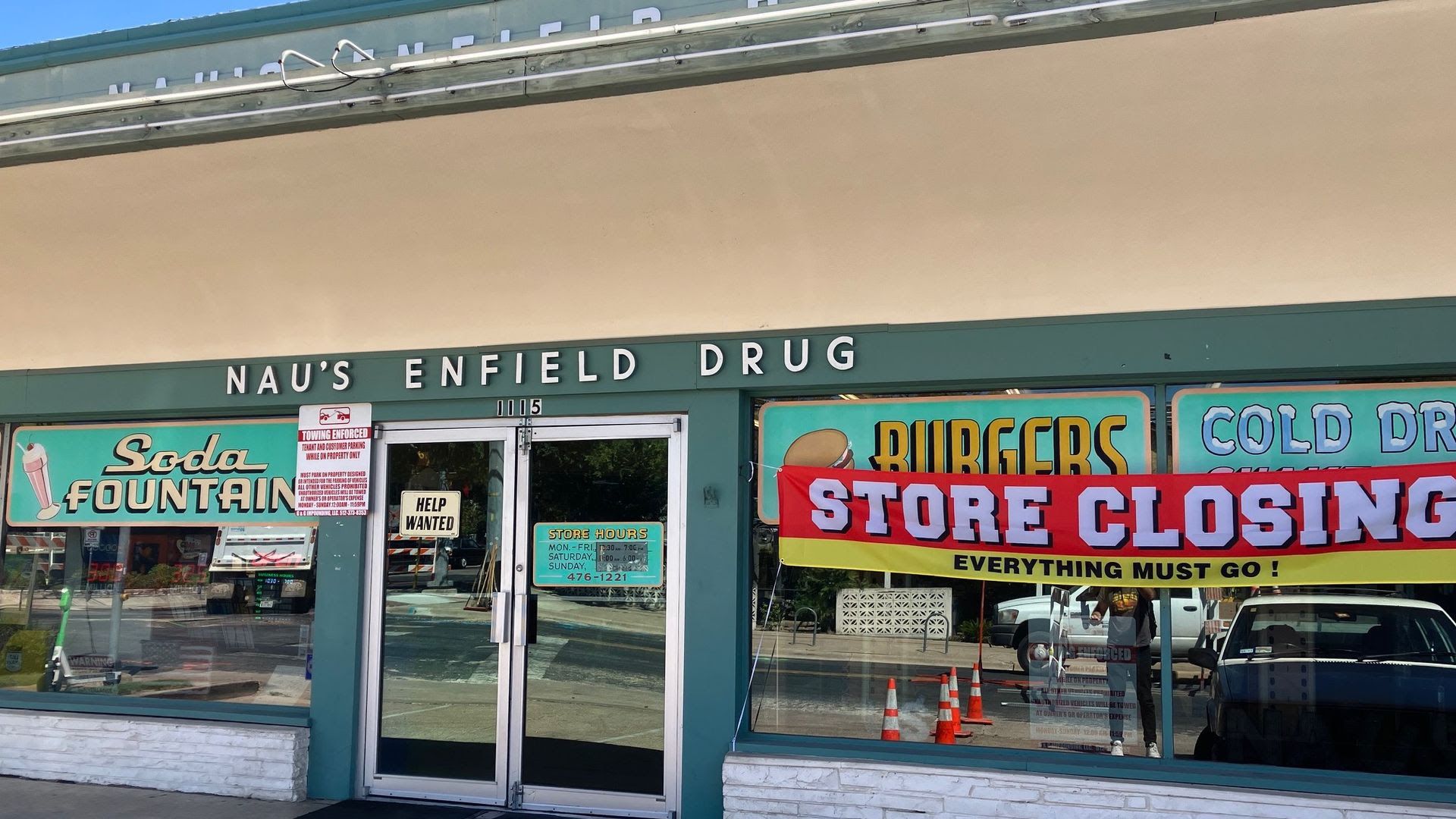 Vintage storefront with teal trim reading NAU'S ENFIELD DRUG; a large "STORE CLOSING" banner, signs for Soda Fountain and Burgers, and a "Help Wanted" sign on the door.