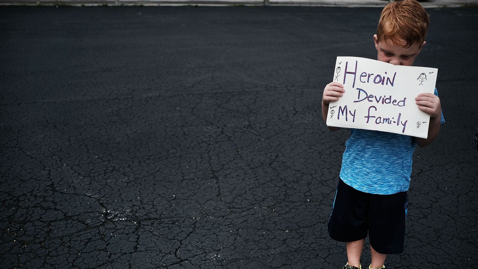 A child holds a sign that says "Heroin divided my family" 