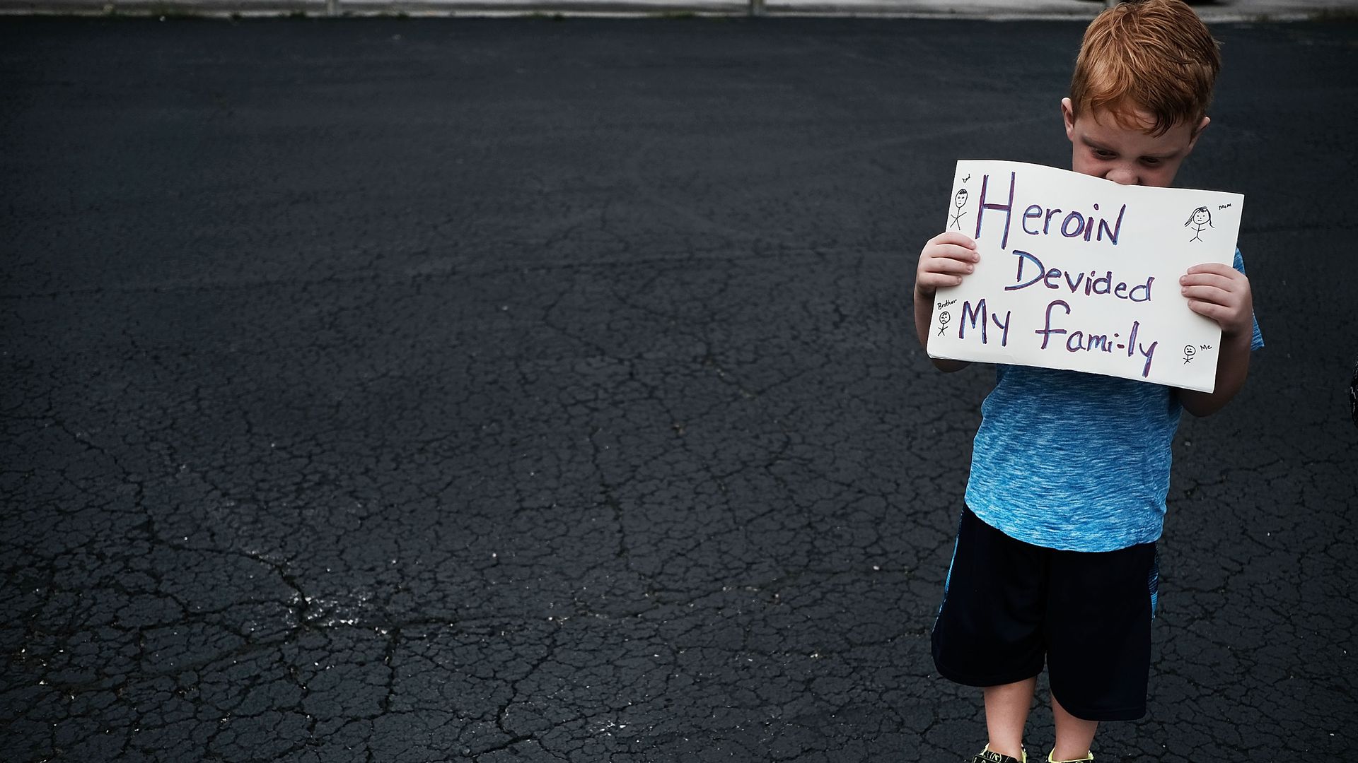 A child holds a sign that says "Heroin divided my family" 