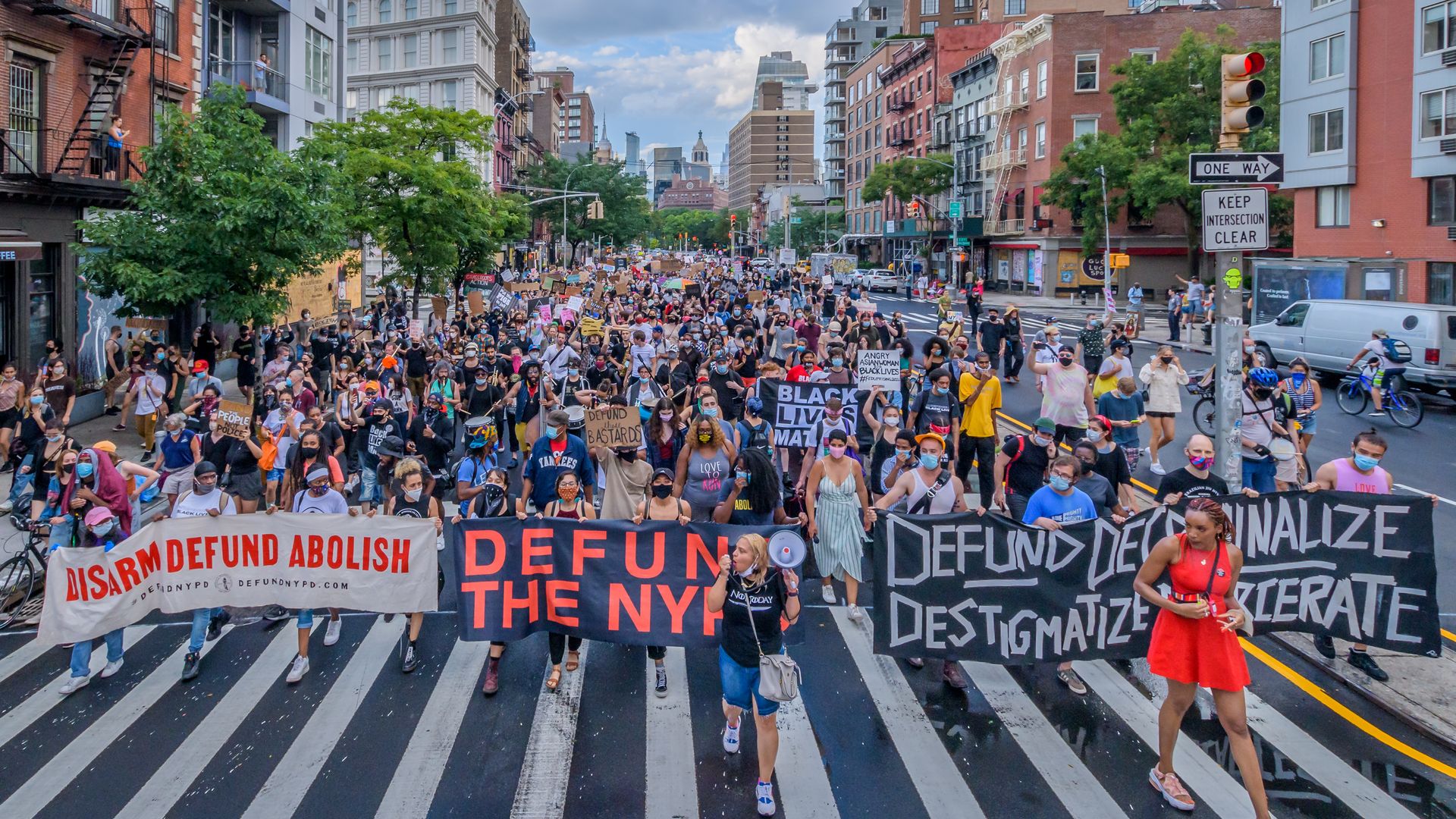 A large crowd holds signs that read "defund the police" and "abolish, disarm"