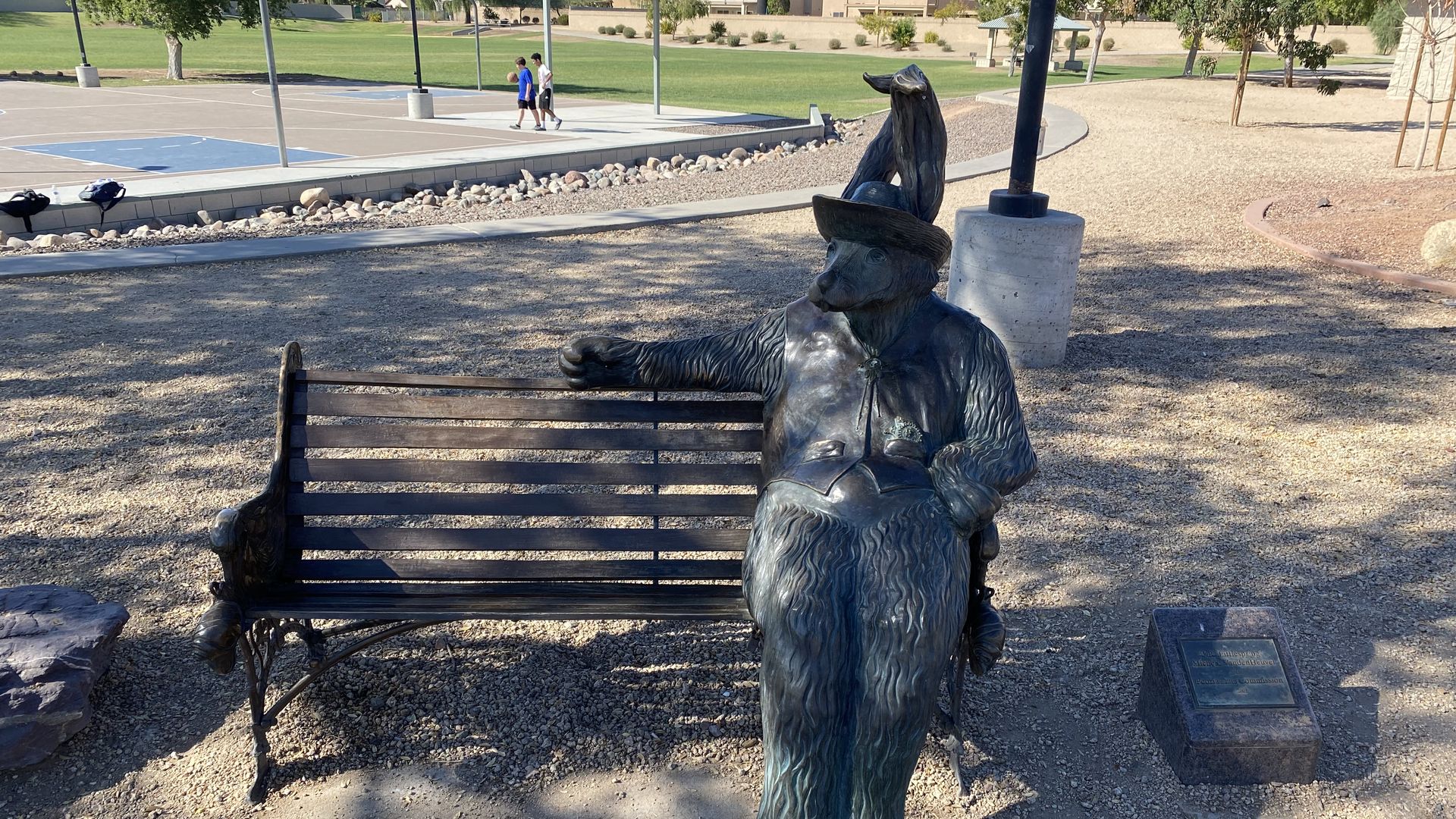An anthropomorphic bronze sculpture of a rabbit in a hat and vest sits on a park bench.