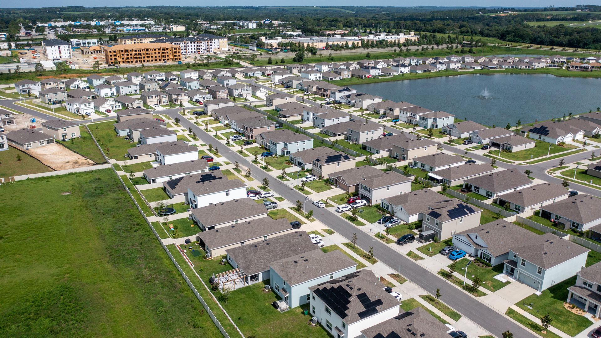 An aerial view of a neighborhood filled with cookie-cutter stucco houses. In the background, a construction site with apartments going up.