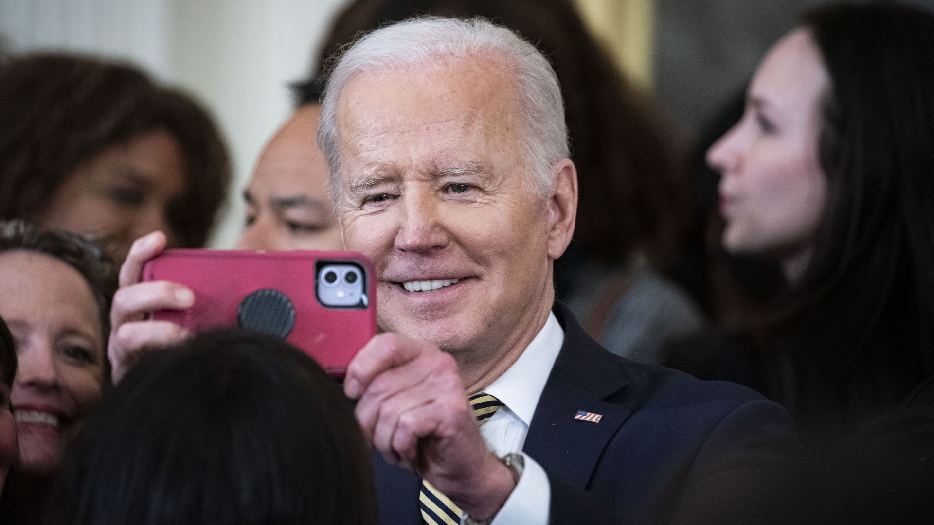 President Biden is seen snapping a photo with an iPhone.