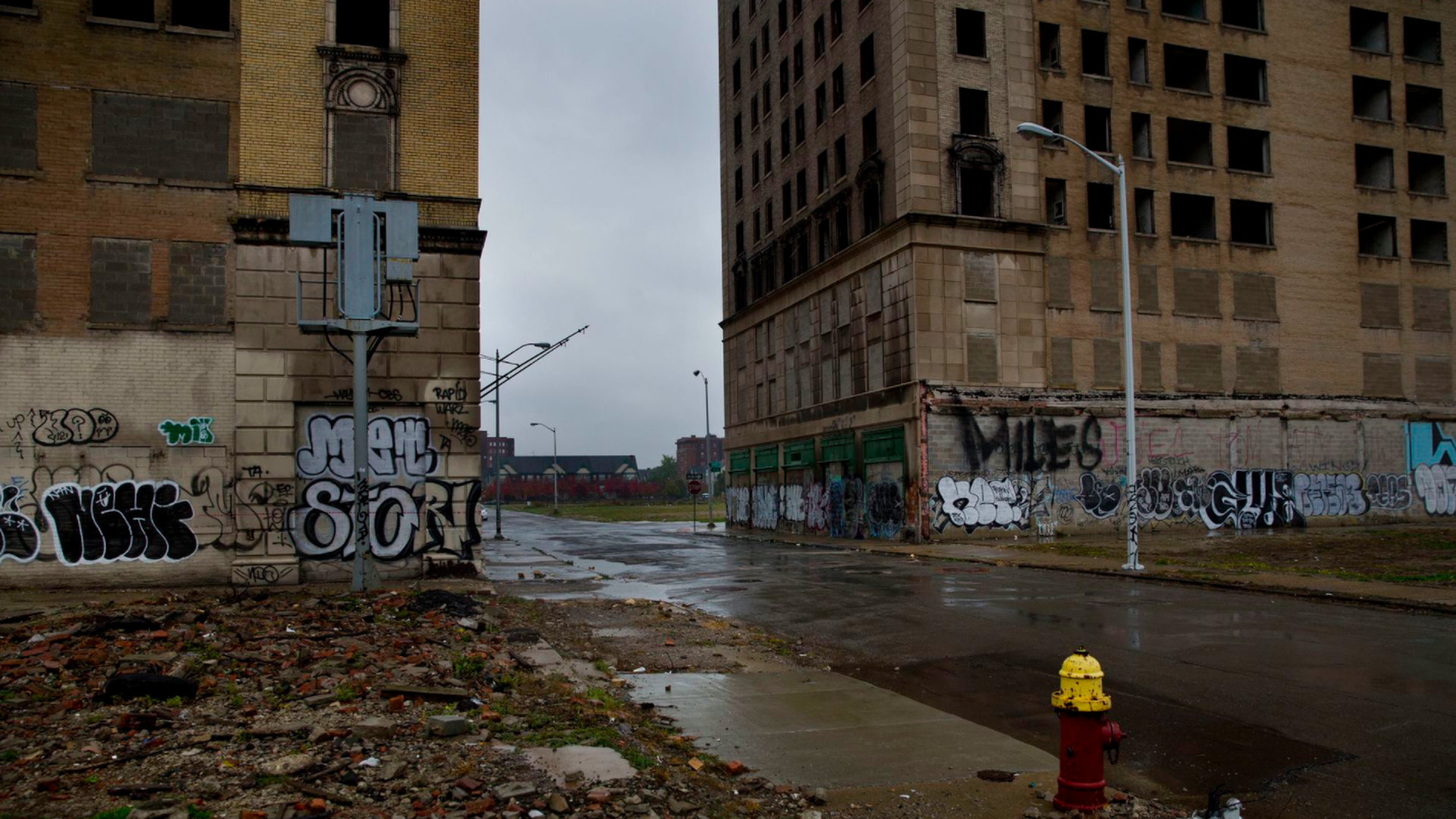 A street on a rainy day surrounded by graffitied buildings