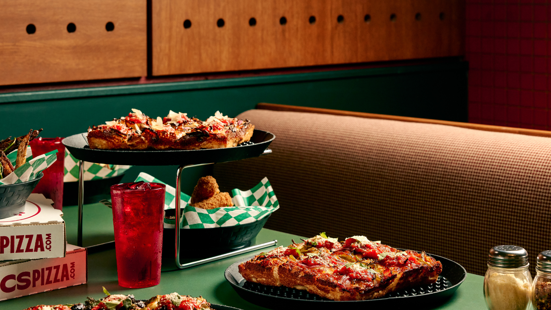 Pizza sitting on a booth at a restaurant, next to pizza boxes and mozzarella sticks