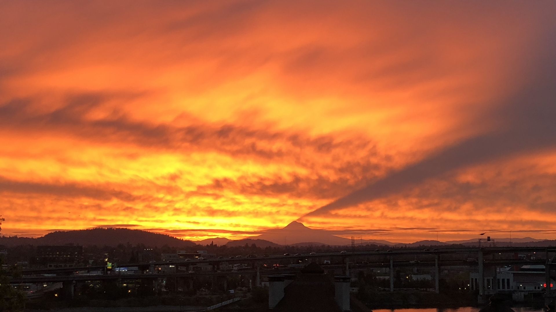 A vivid sunrise casts a shadow off a mountain into the bright orange and yellow clouds.