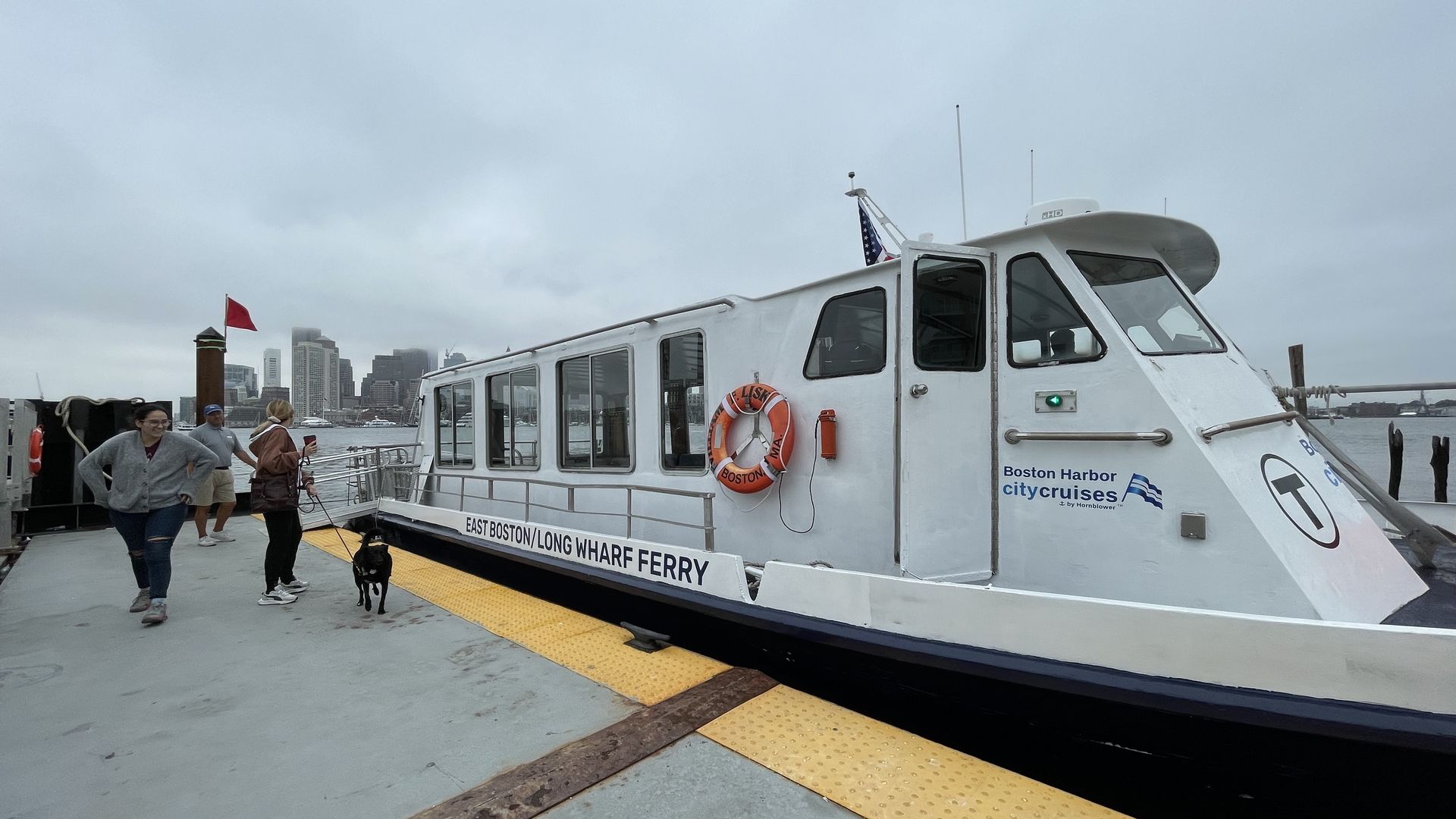 The East Boston ferry lands at a pier in Eastie, and a transit employee moves the ramp off the pier onto the train after two passengers and a dog get off.