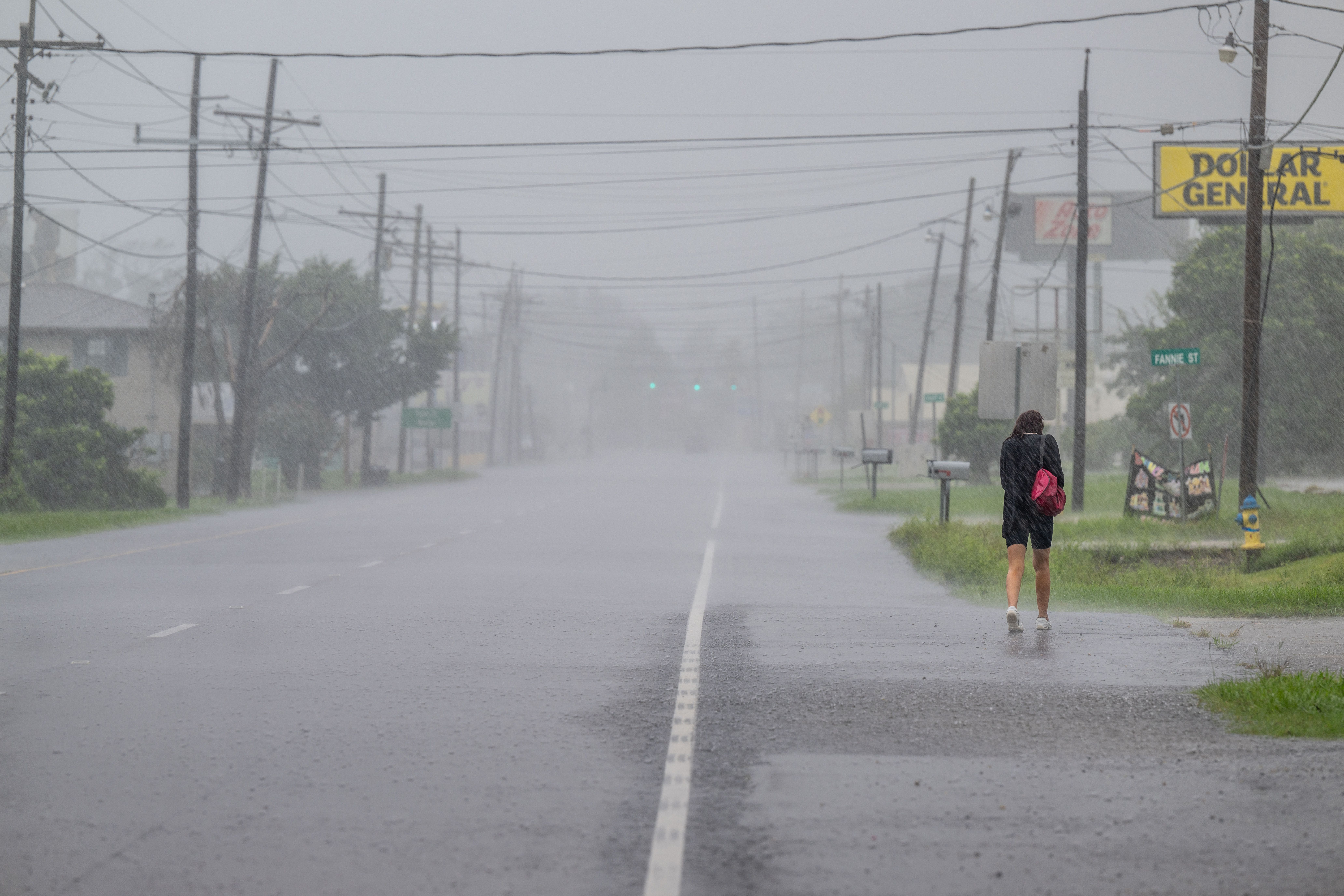 A person hunches over as they walk along a rainy street.