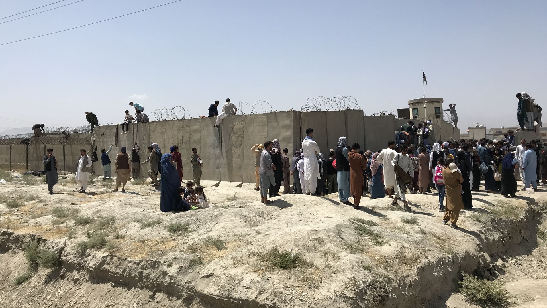 People try to climb over the walls onto the grounds of Hamid Karzai International Airport in the hopes of evacuating
