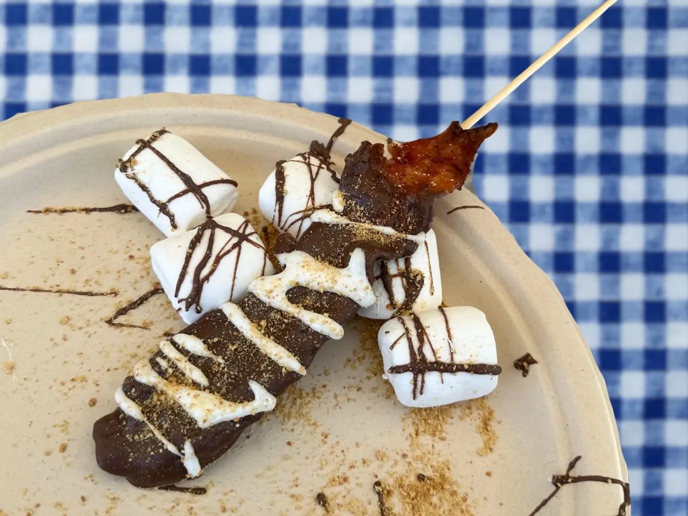 Bacon covered in chocolate on a paper plate with large marshmallows. 