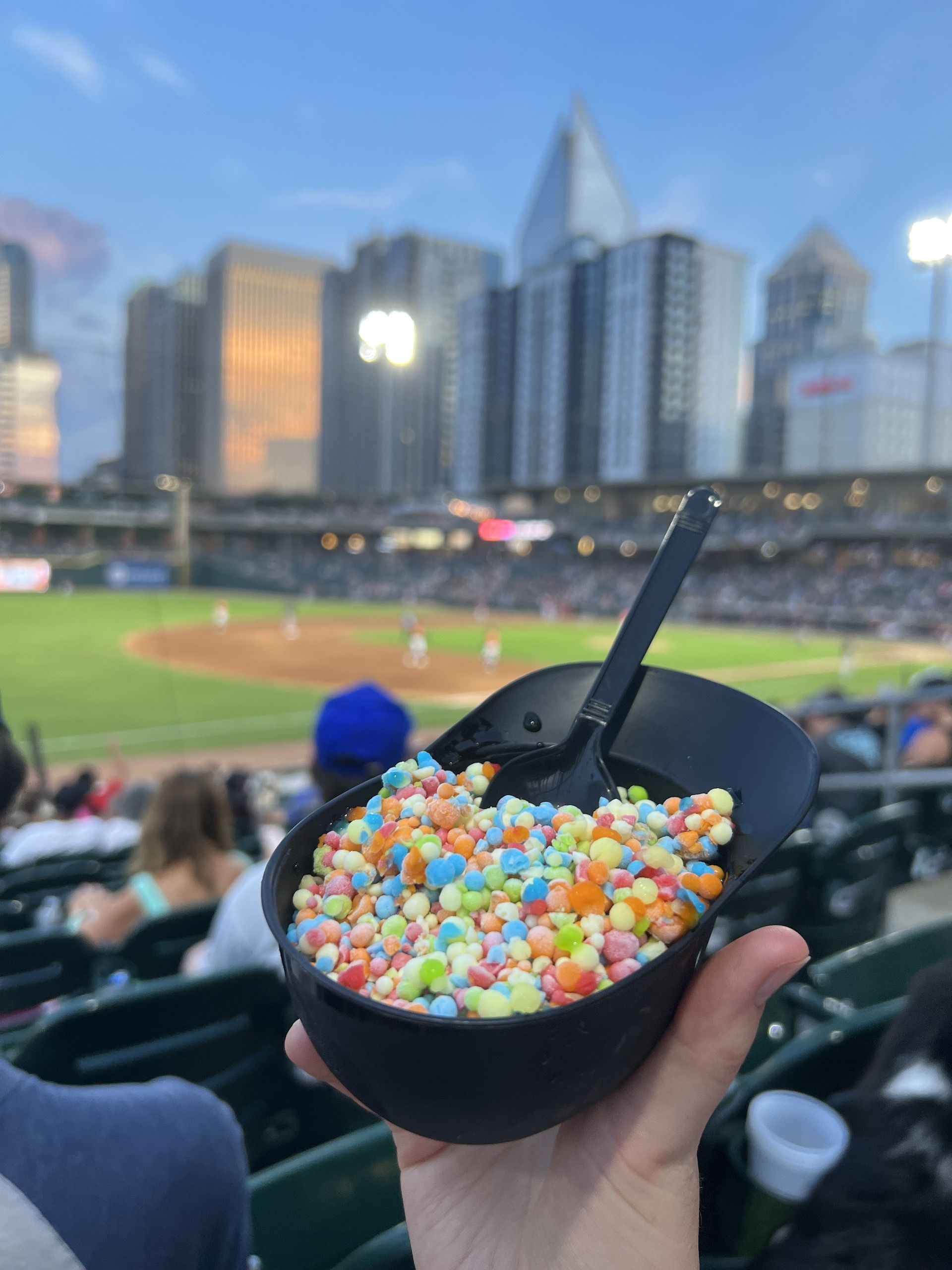 Dipping dots in a hand-sized baseball cap, in front of a baseball stadium field. 
