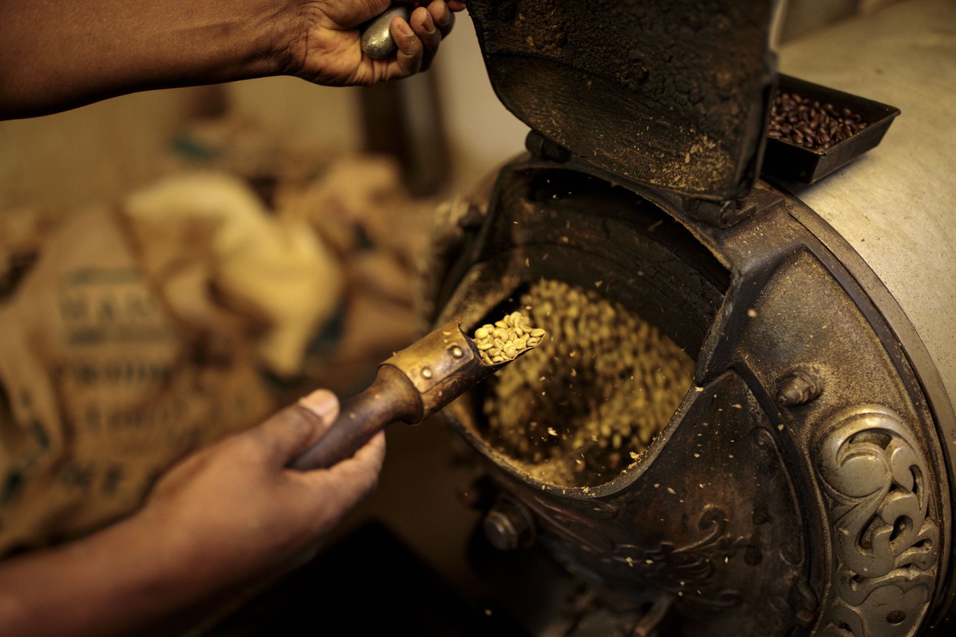 A person holds a shaped spoon toward a small coffee roaster.