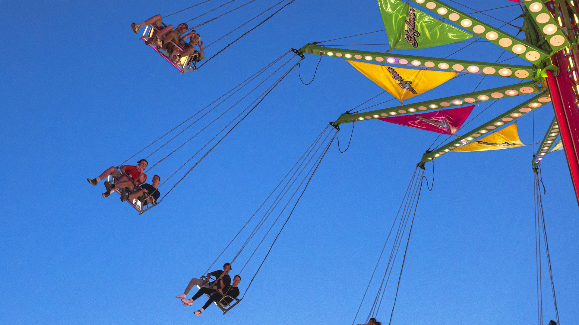 Colorful swing ride at a fair with people enjoying the ride against a clear blue sky at dusk.