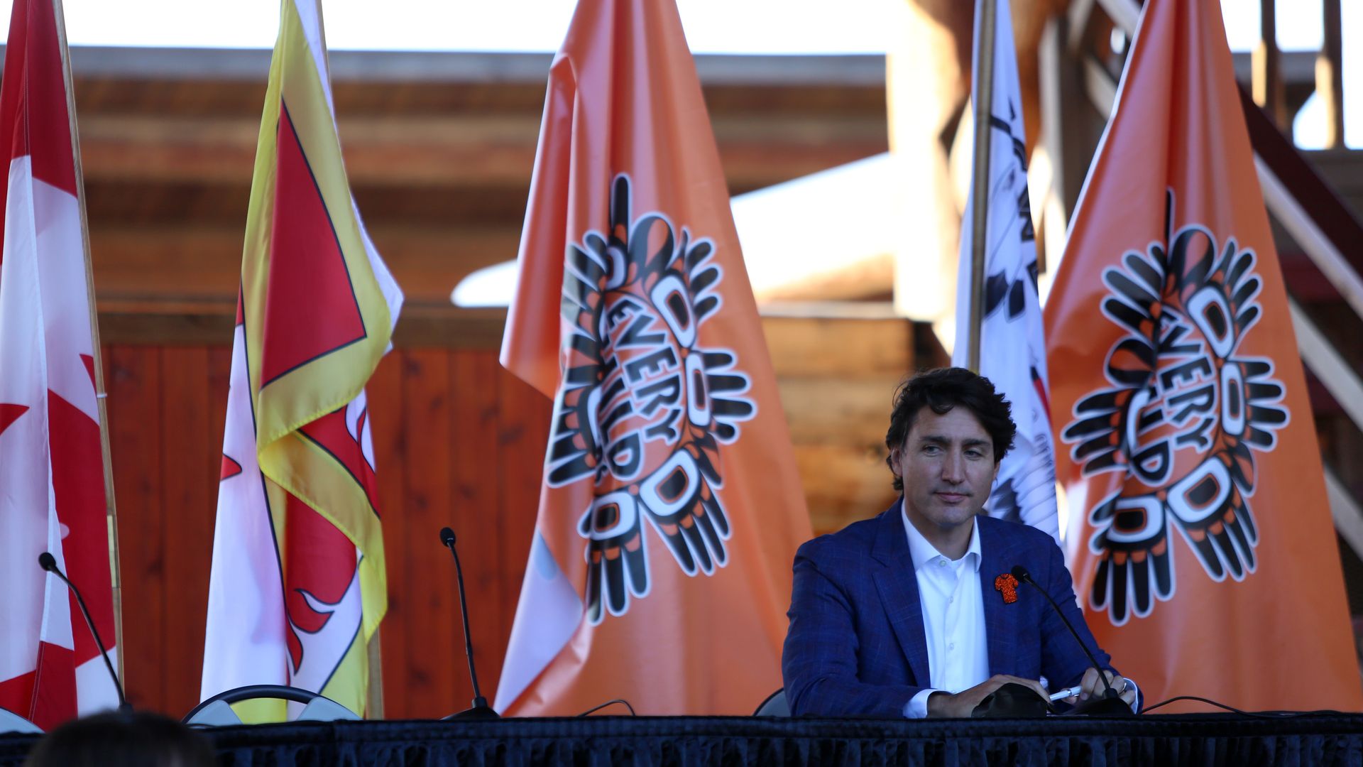 Photo of Justin Trudeau sitting with flags that say "Every Child Matters" standing behind him