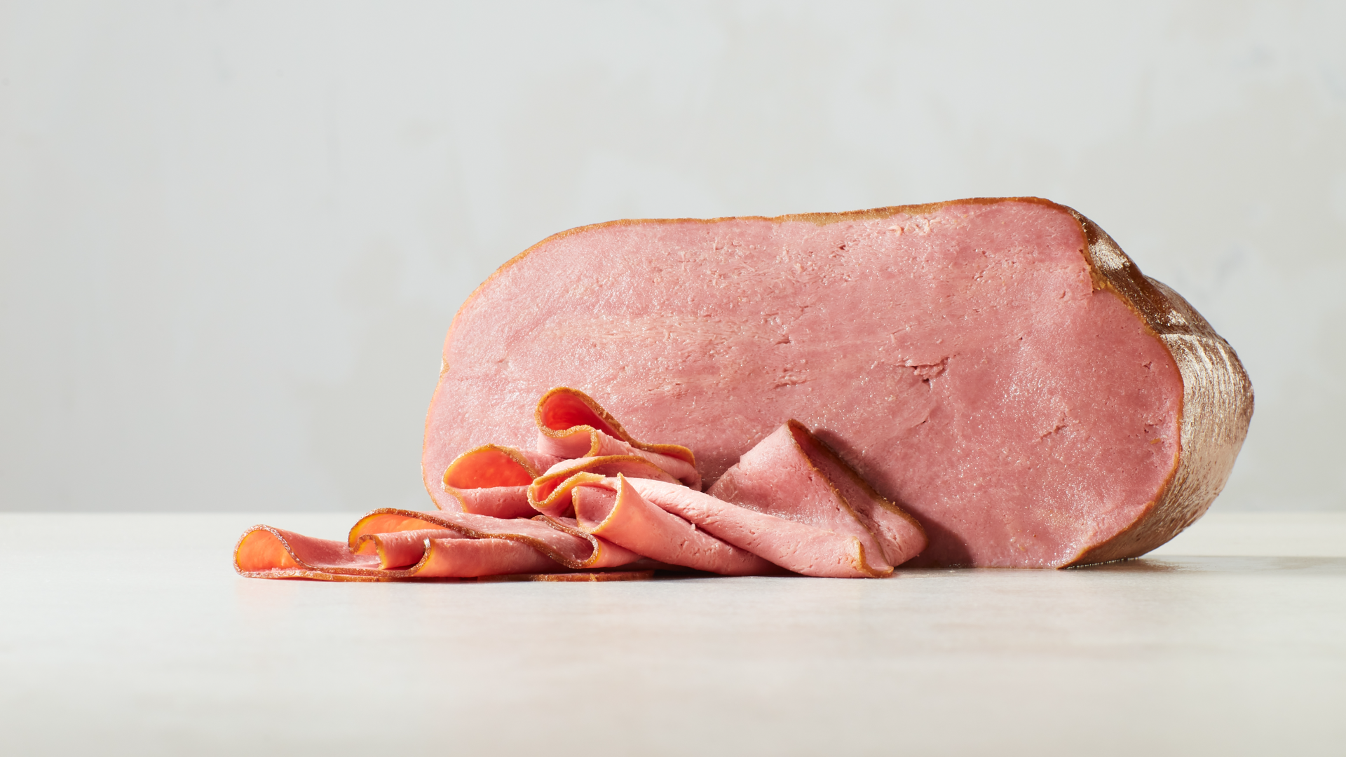 A photo of plant-based ham produced by Project Eaden, sitting on a wooden cutting board against a light background.