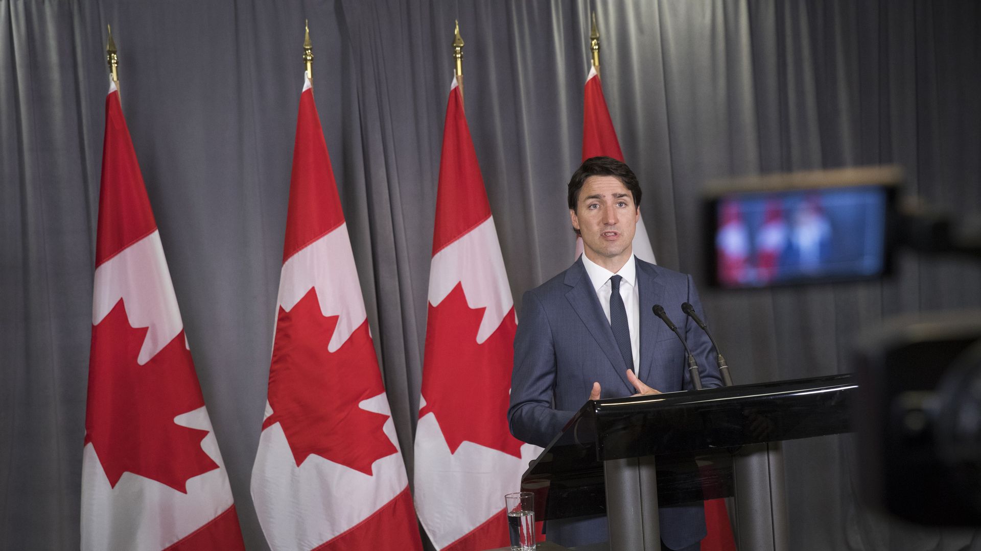 Justin Trudeau speaks at podium before four Canadian flags.