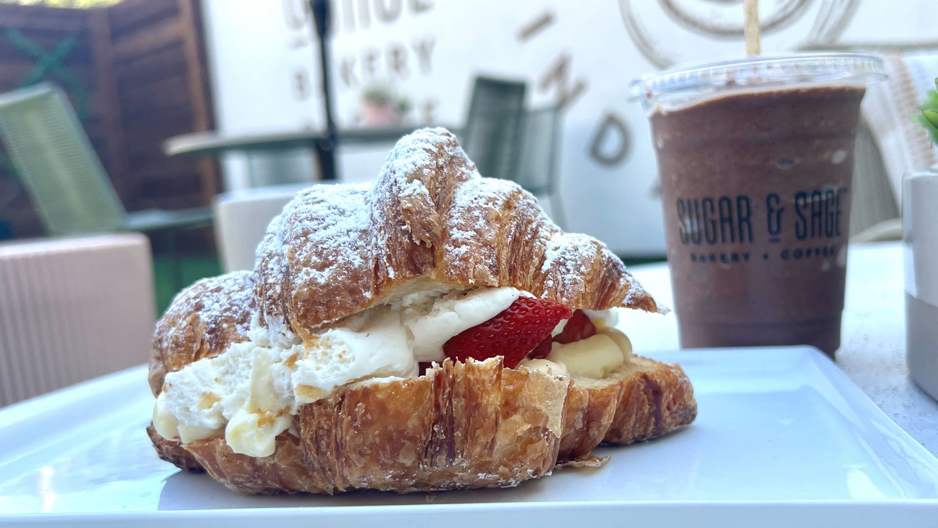 A photo of a stuffed croissant with strawberries and a frozen hot chocolate in the background