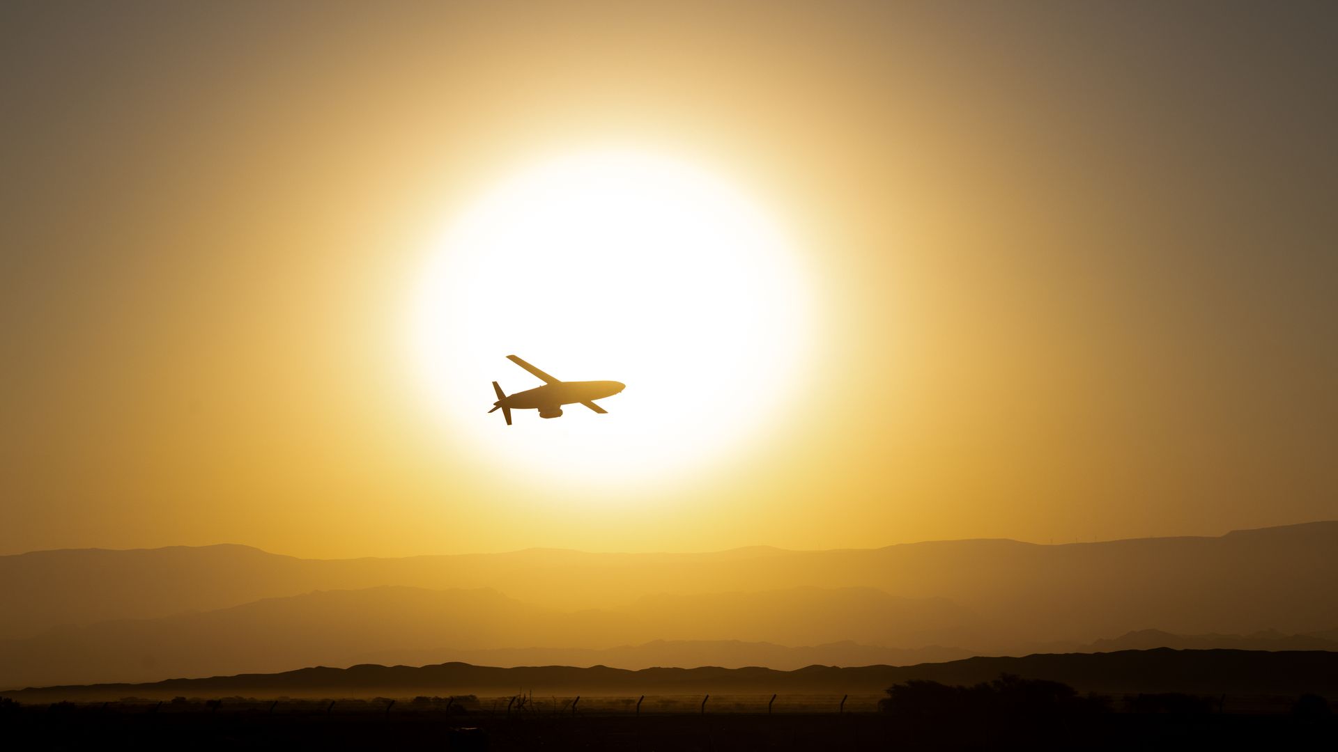 A missile zips through the sky, set against a sunset. The ground is seen in the lower fourth of the photo.