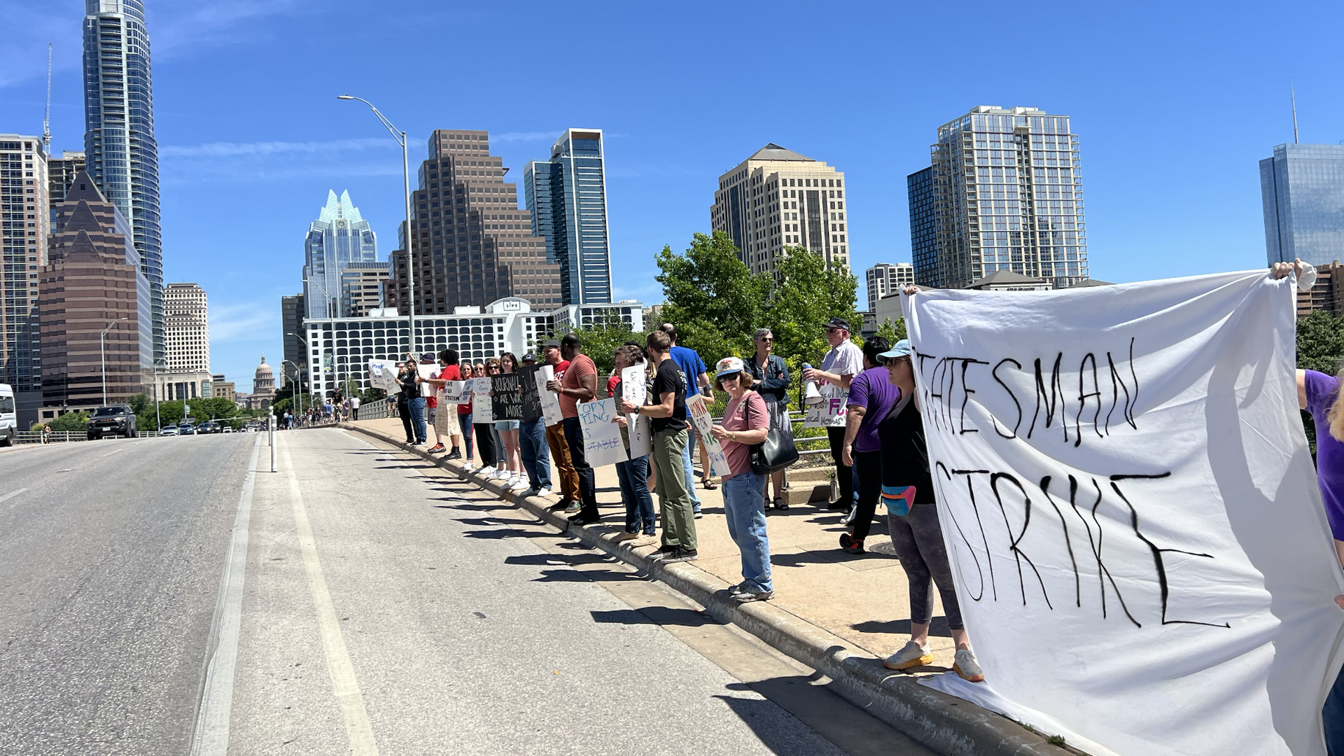 A photo of workers in a row on a bridge with the skyline in the background.