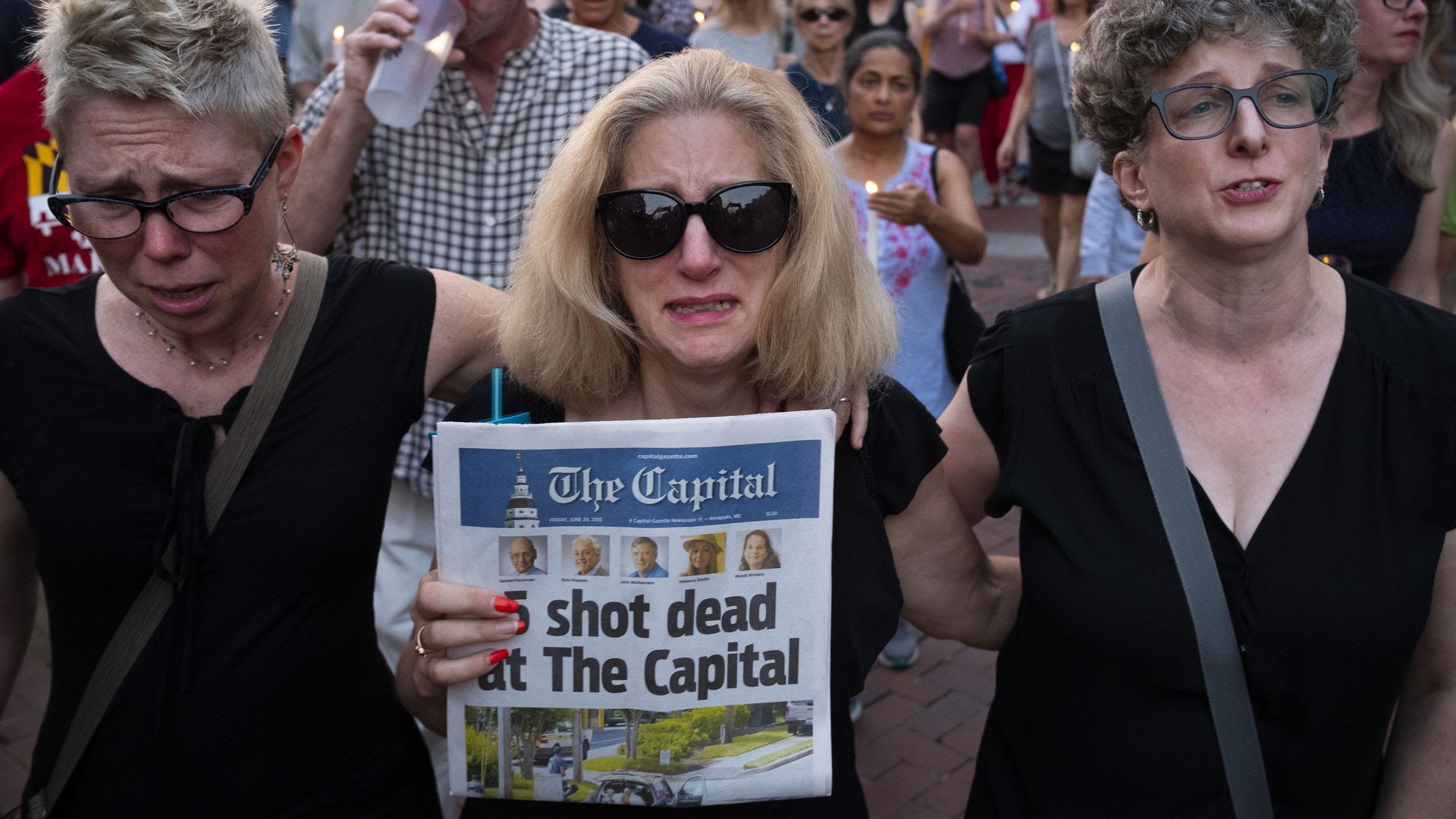 A woman holds a newspaper showing deaths at a newsroom in Maryland.
