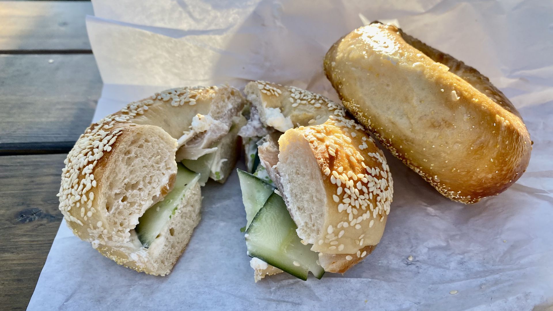 A bagel sandwich halved, with cucumber and fish, next to a plain bagel. 