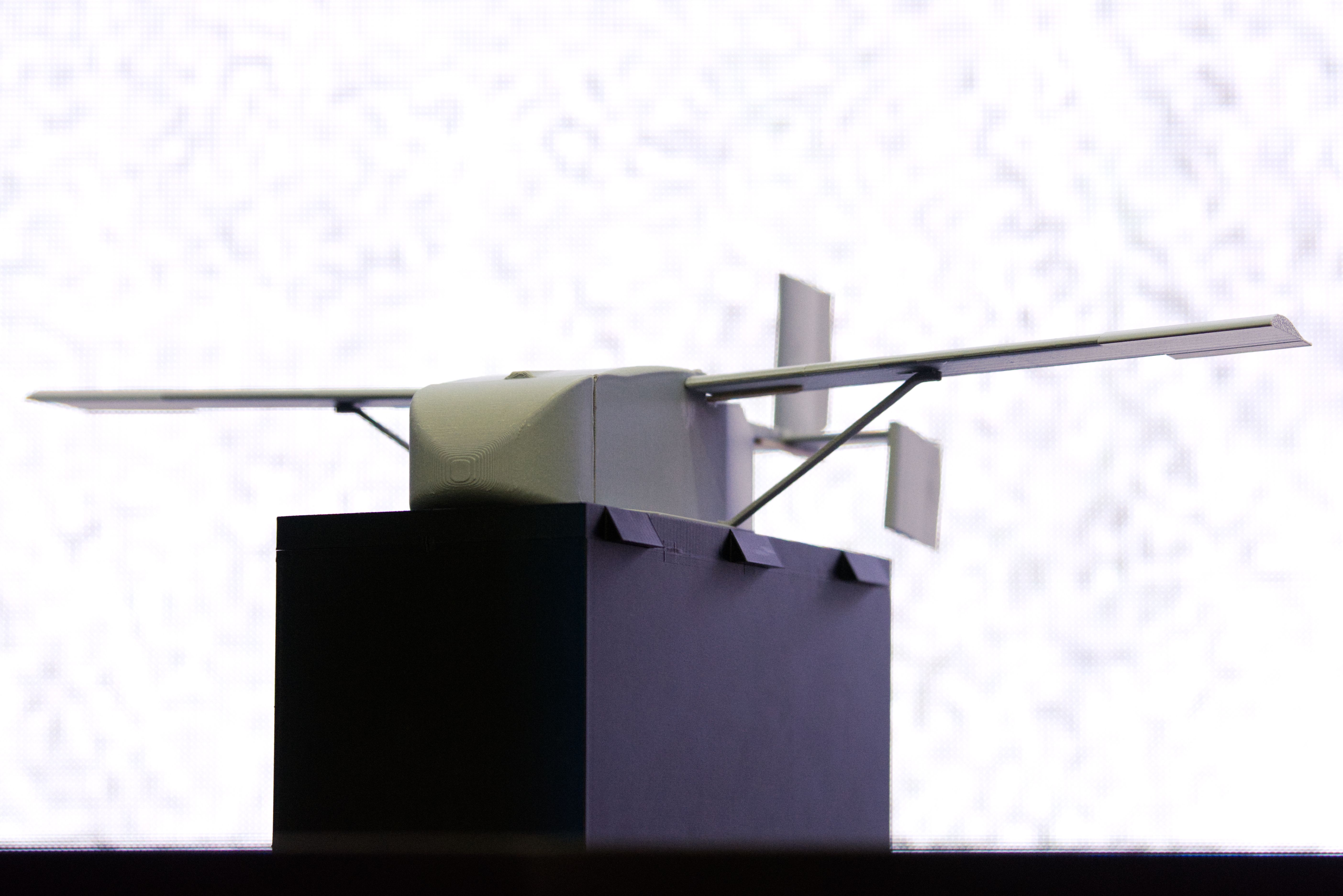 A small model of the Grasshopper cargo drone. It sits on a black box. The background is static.