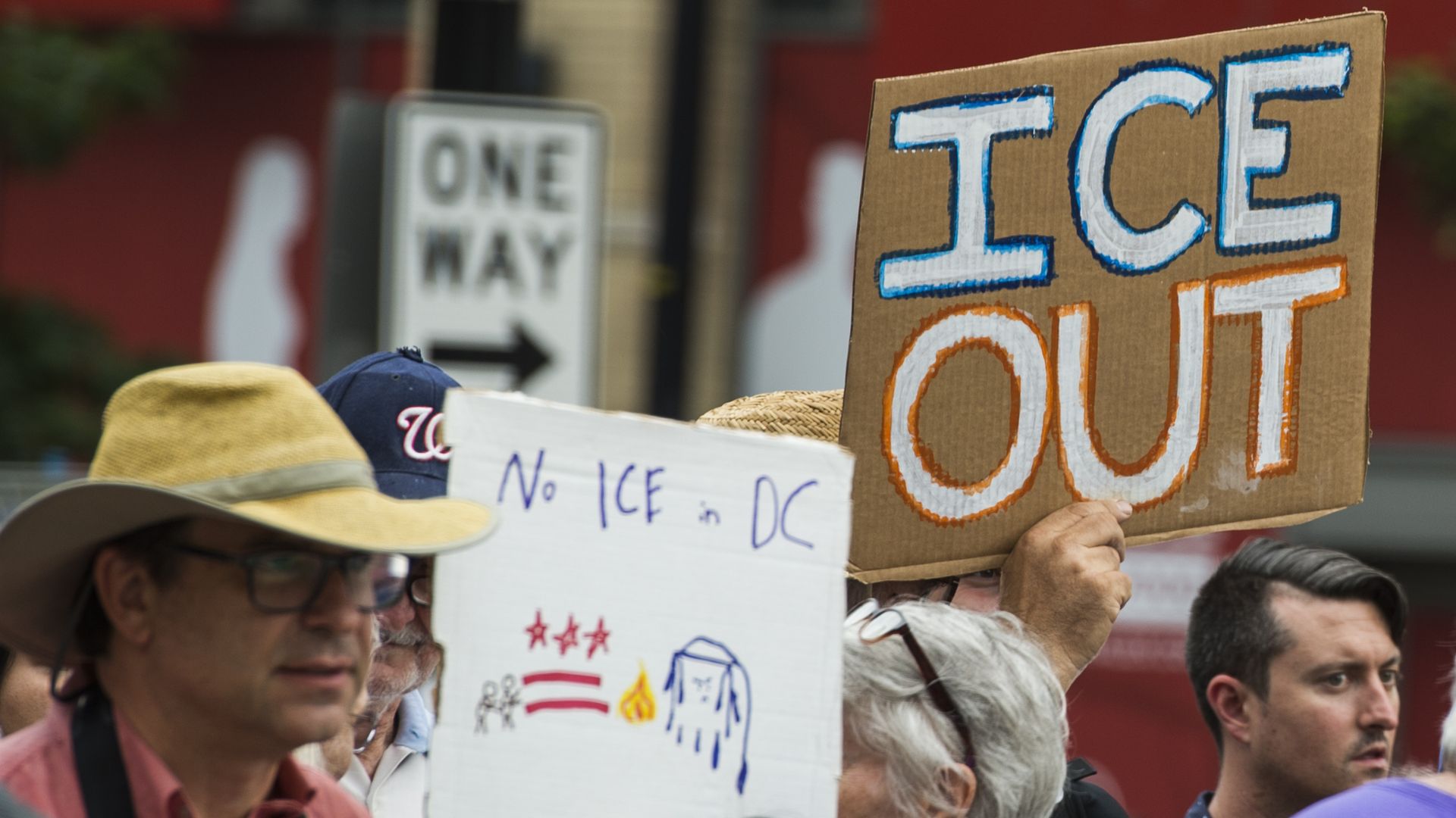 This image shows someone holding a sign that reads "ICE OUT" in a crowd.