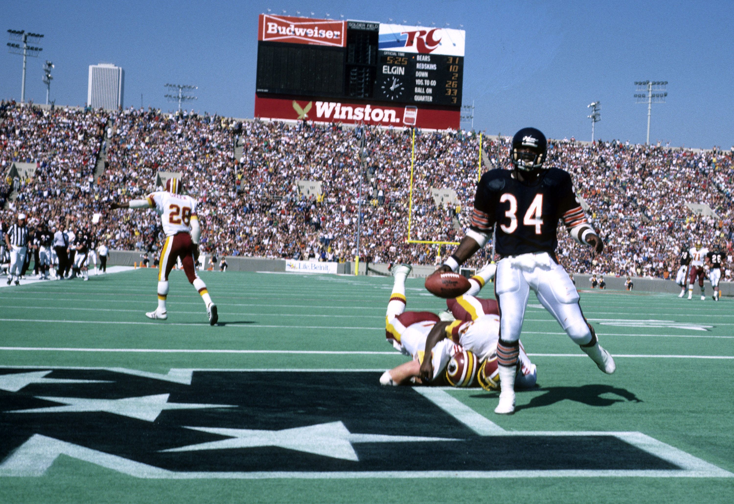 Photo of a football player scoring a touchdown with a scoreboard and thousands of fans in a stadium. 