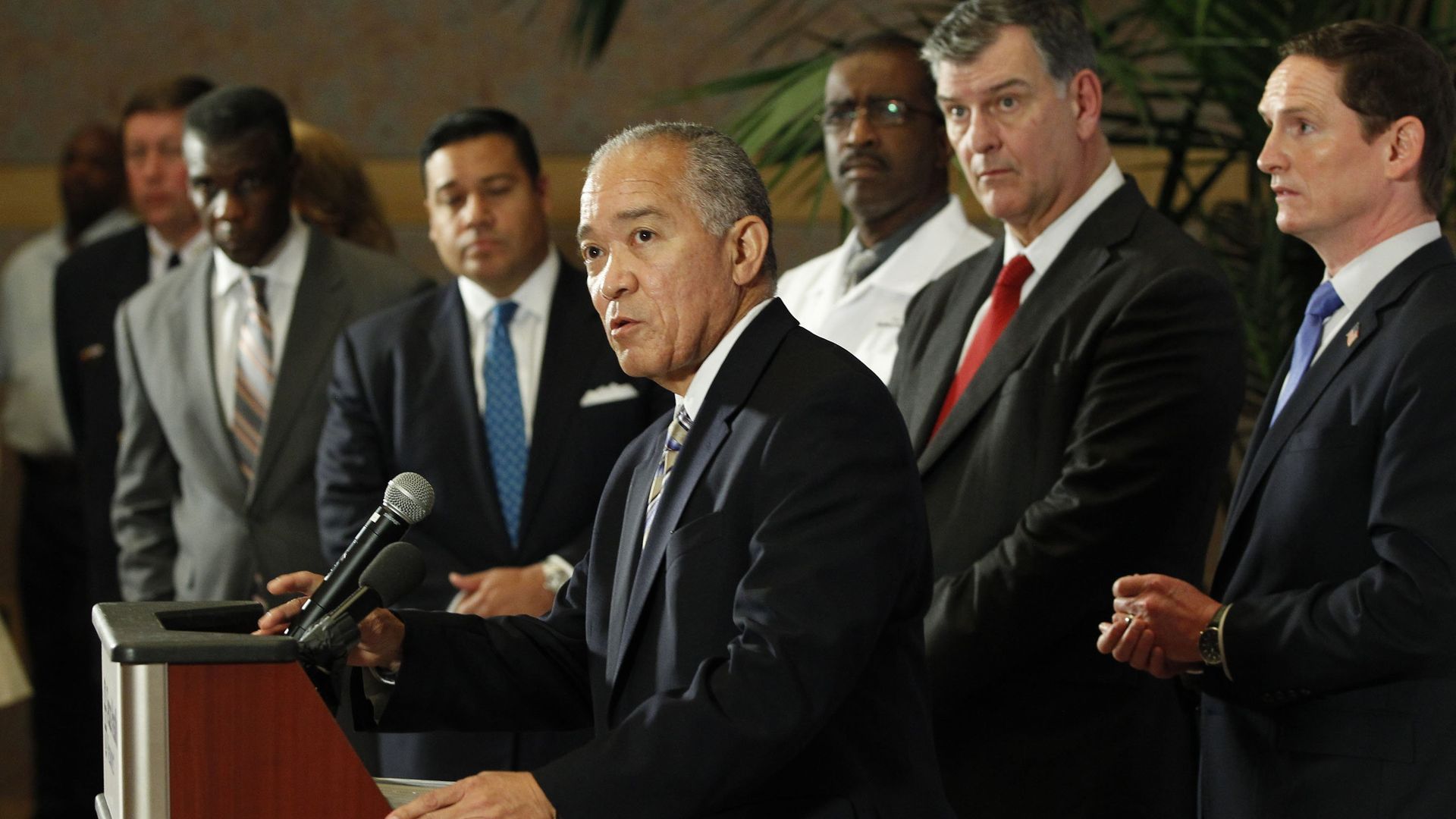 A man in a suit at a podium, surrounded by other men in suits.